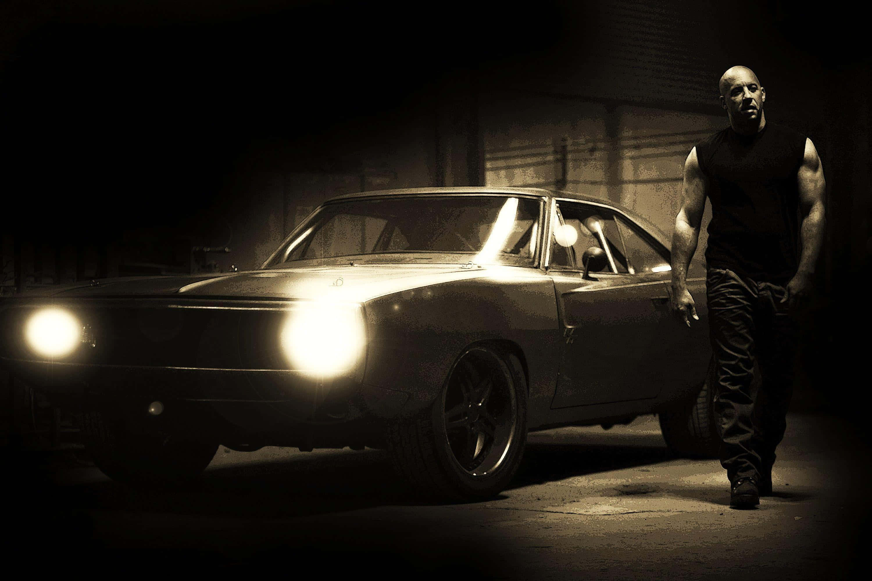 Fast And Furious 1 桌布 壁紙 — 一個肌肉發達的男人站在一輛帶有發光車頭燈的復古肌肉車旁，車庫光線昏暗。