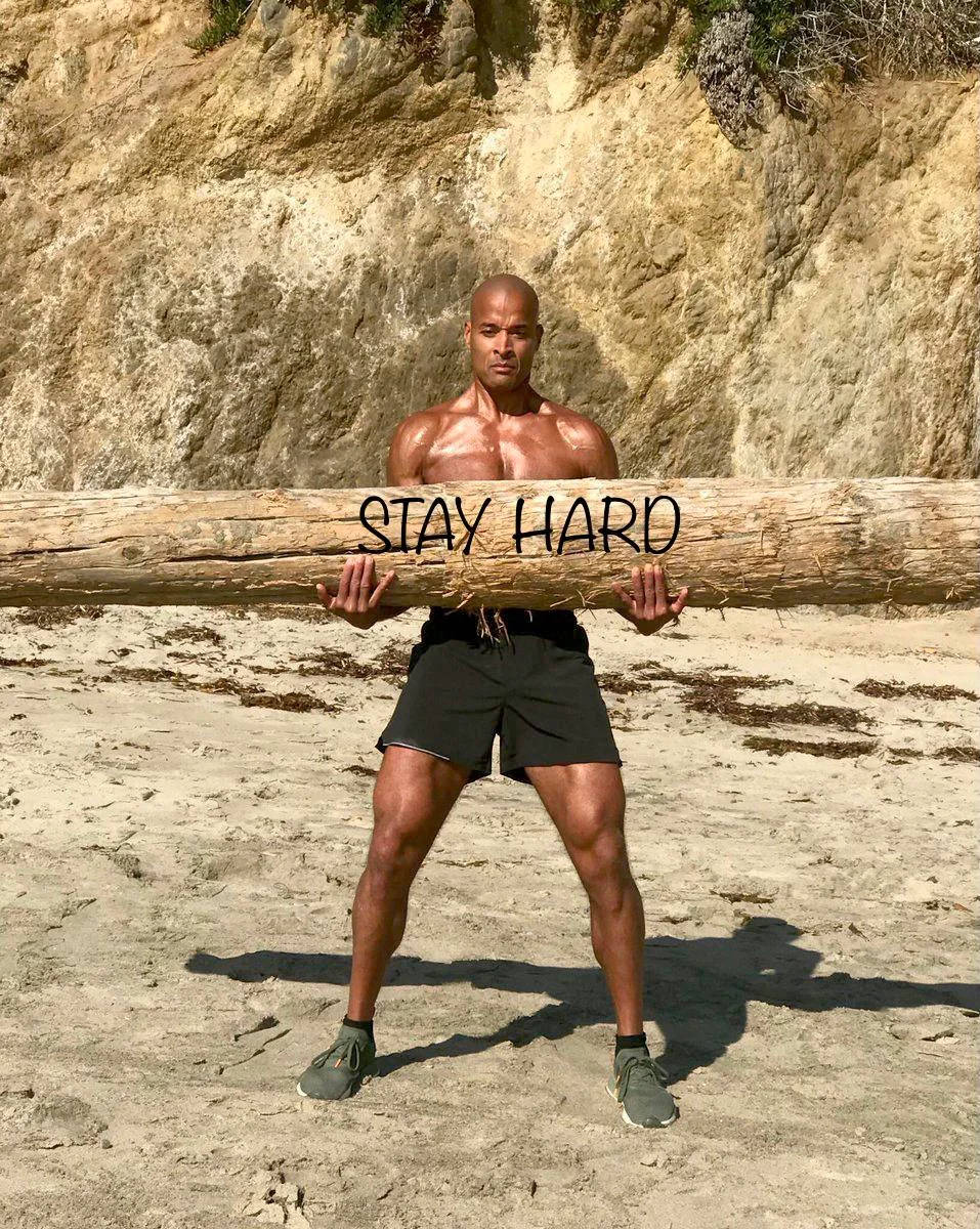 一個健美的男人在陽光海灘上靠近懸崖處手持寫有'STAY HARD'的木頭。 — 勵志動圖 壁紙