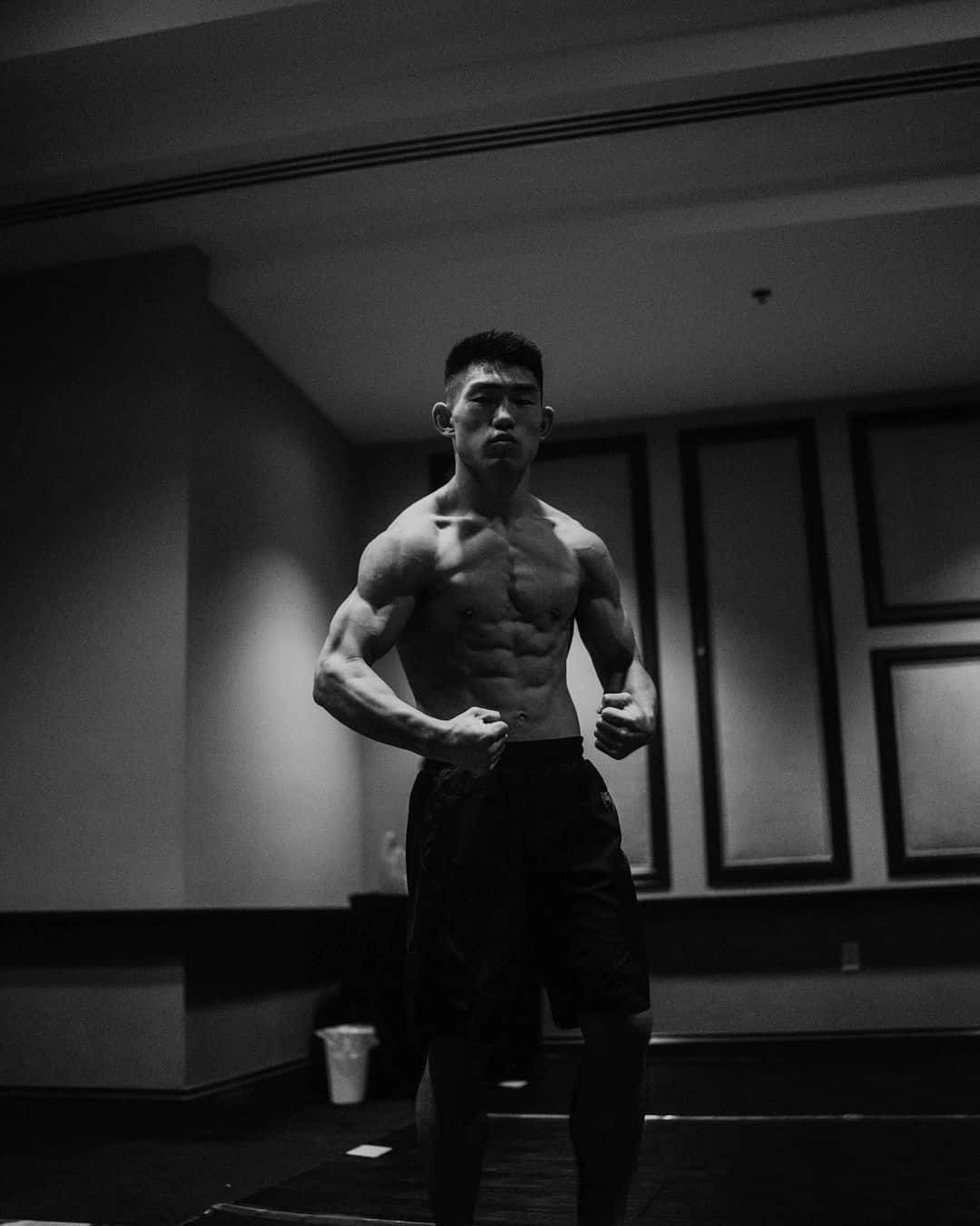 Black And White Portrait 桌布 壁紙 — 一個肌肉發達的男人赤膊站在燈光昏暗的房間裡，腹肌分明，眼神專注。