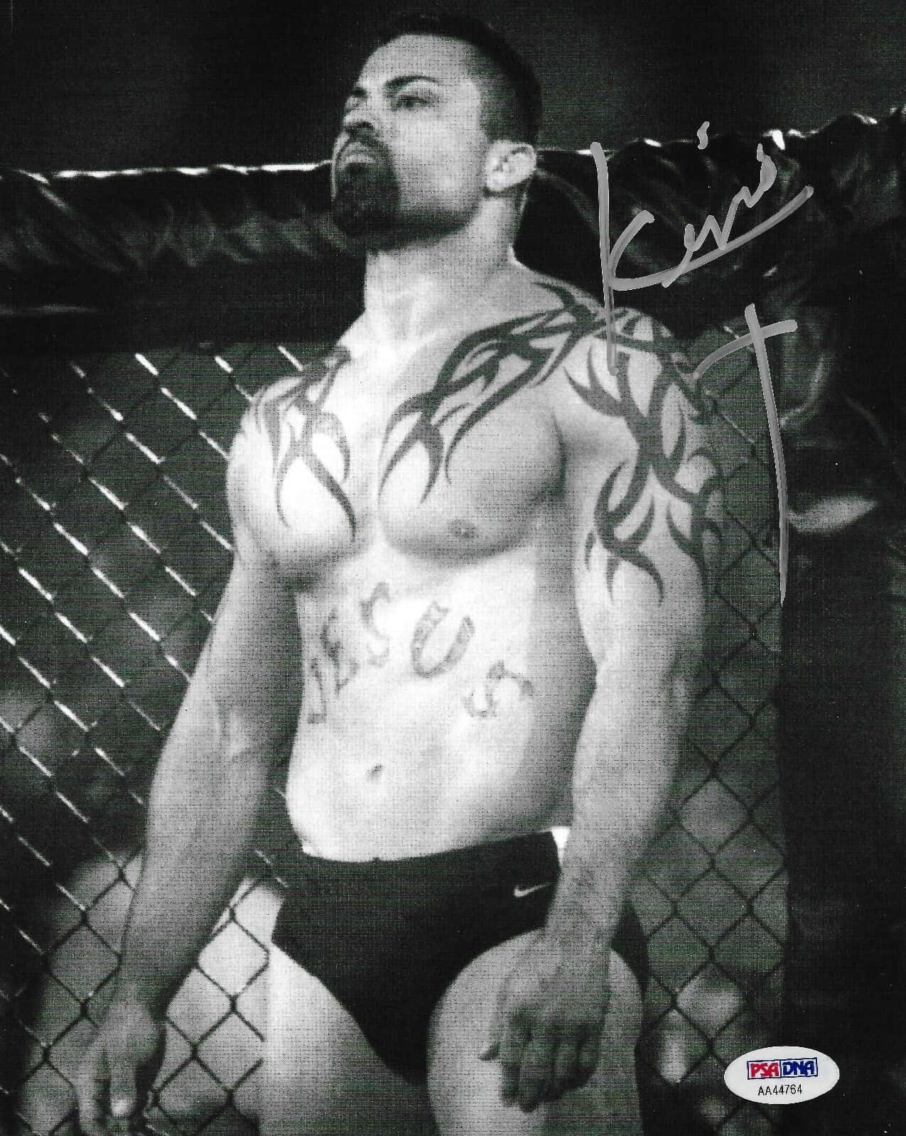 UFC 桌布 壁紙 — 一個肌肉發達的男子，身上有部落紋身，胸前有 'jesus' 字樣，站在鐵絲網籠中的黑白照片。