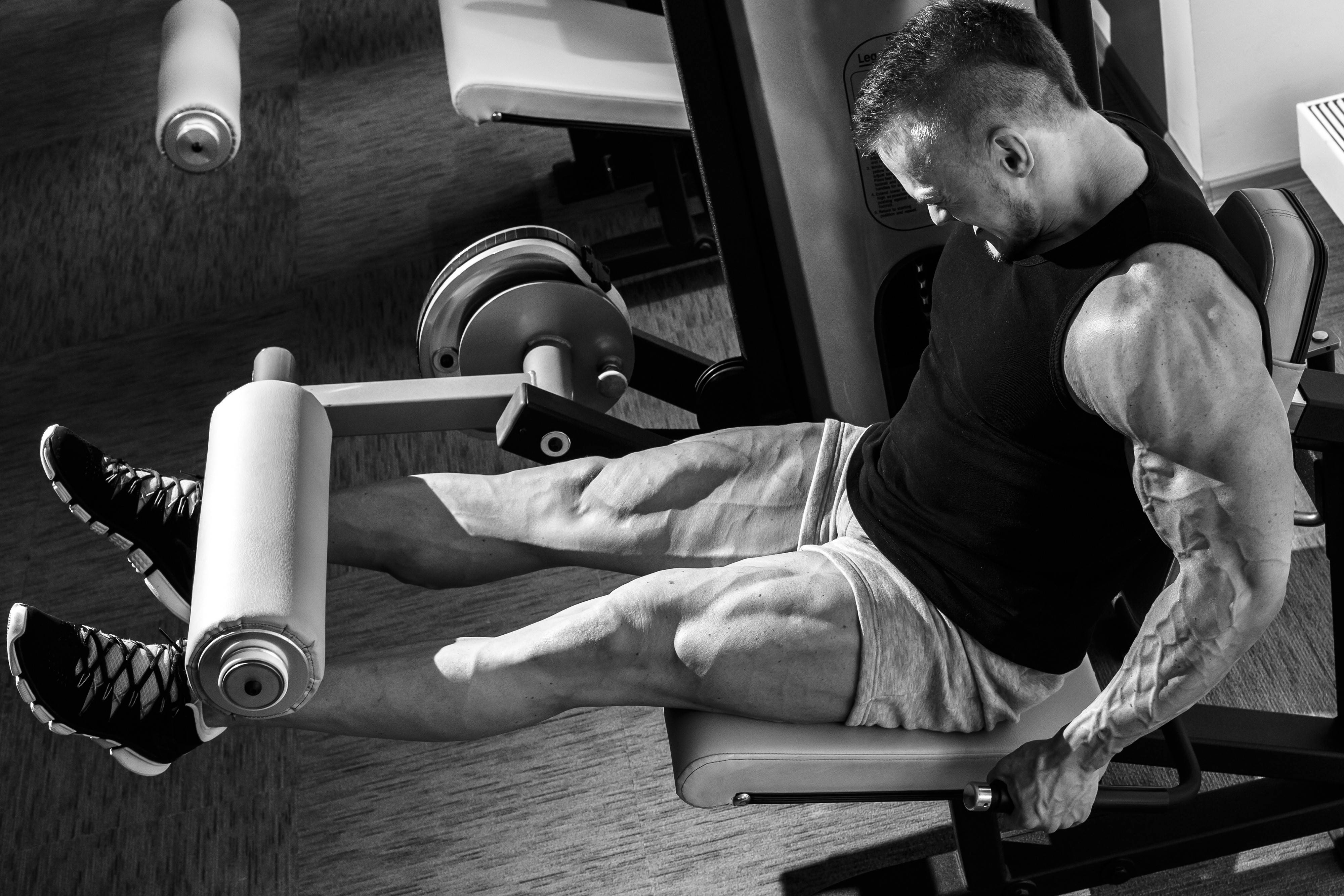 Exercise 桌布 壁紙 — 一個肌肉發達的男子在健身房中於腿部推舉機上劇烈鍛煉，以高對比度黑白捕捉。