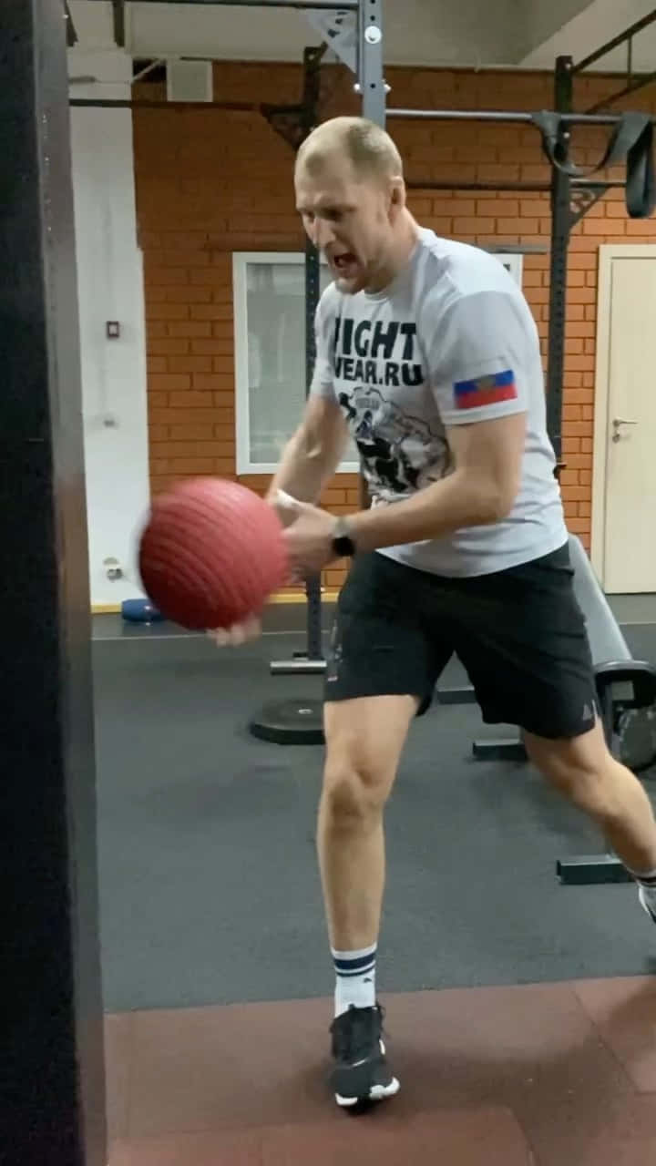 Athletic 桌布 壁紙 — 一個肌肉發達的男子在健身房專注地準備擲出一個紅色藥球，充滿決心。