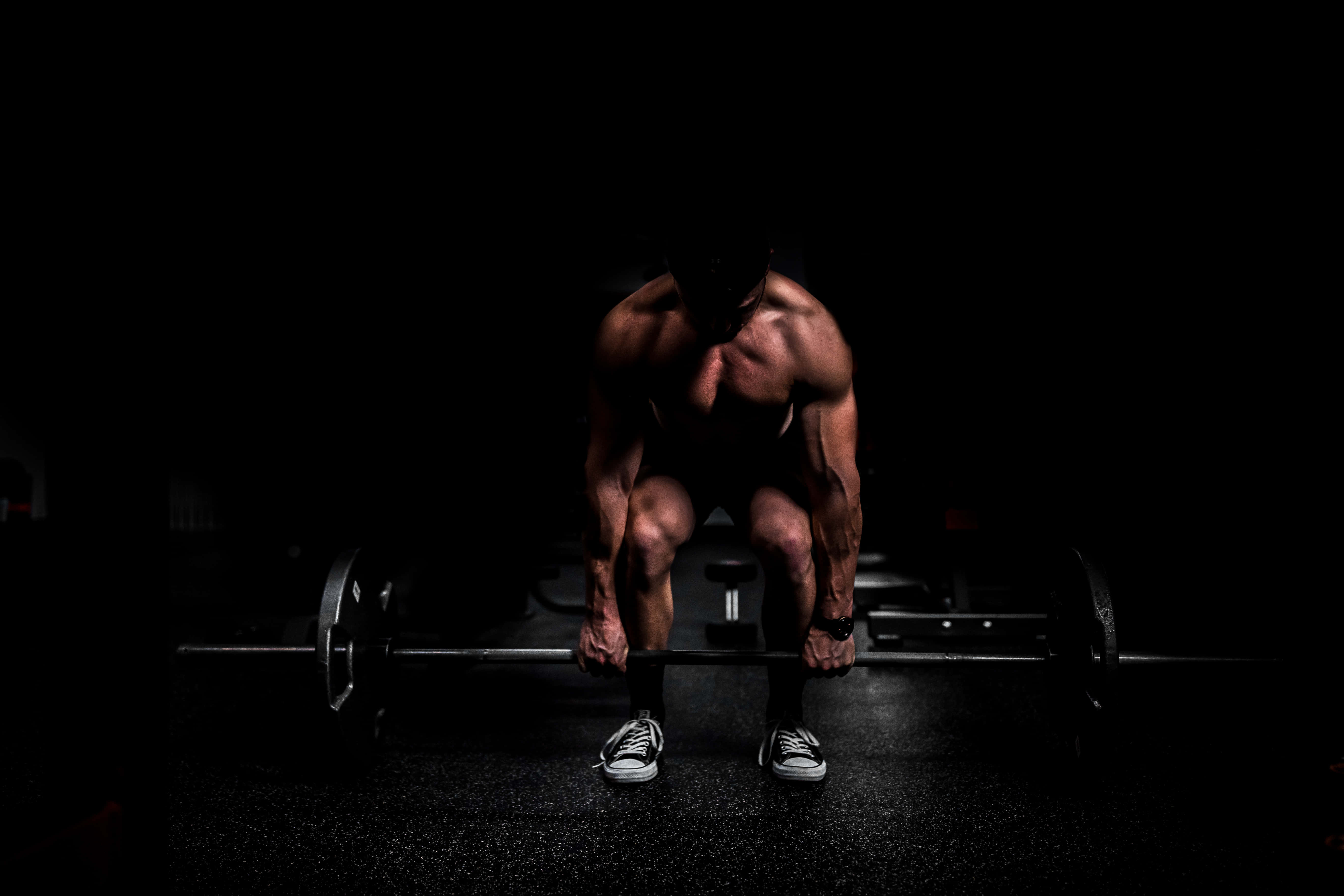 Exercise 桌布 壁紙 — 一個肌肉發達的男子在昏暗的健身房中，在戲劇性的聚光燈下，緊張地準備舉起沉重的槓鈴。