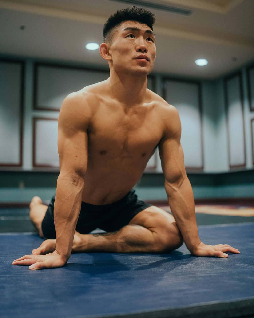 瑜珈 桌布 壁紙 — 一個肌肉發達的男子在柔和光線的健身房內，在藍色瑜伽墊上專注地做瑜伽姿勢。