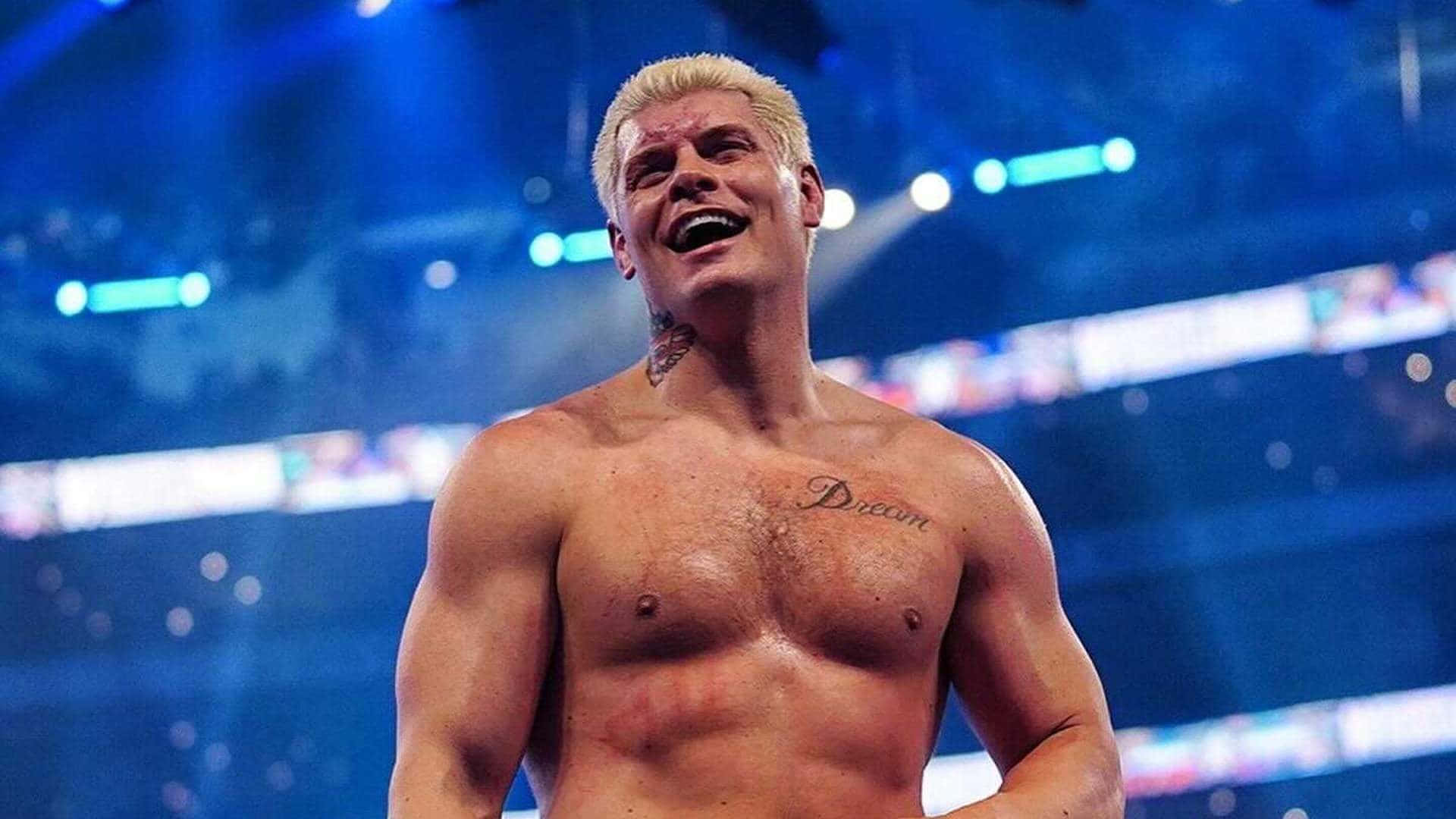 WWE 桌布 壁紙 — 一個肌肉發達的金髮摔角手在燈光明亮的競技場中勝利大笑，背景有藍色燈光和模糊的人群。