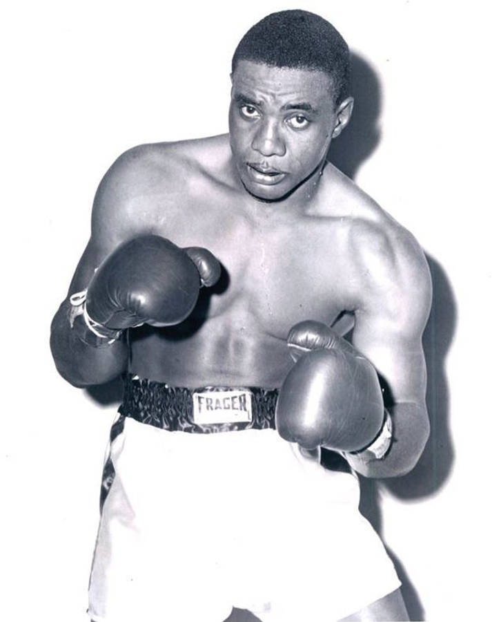 Boxing 桌布 壁紙 — 一個肌肉發達的黑人拳擊手，身穿復古裝備，在純白背景前舉起拳頭，眼神銳利。