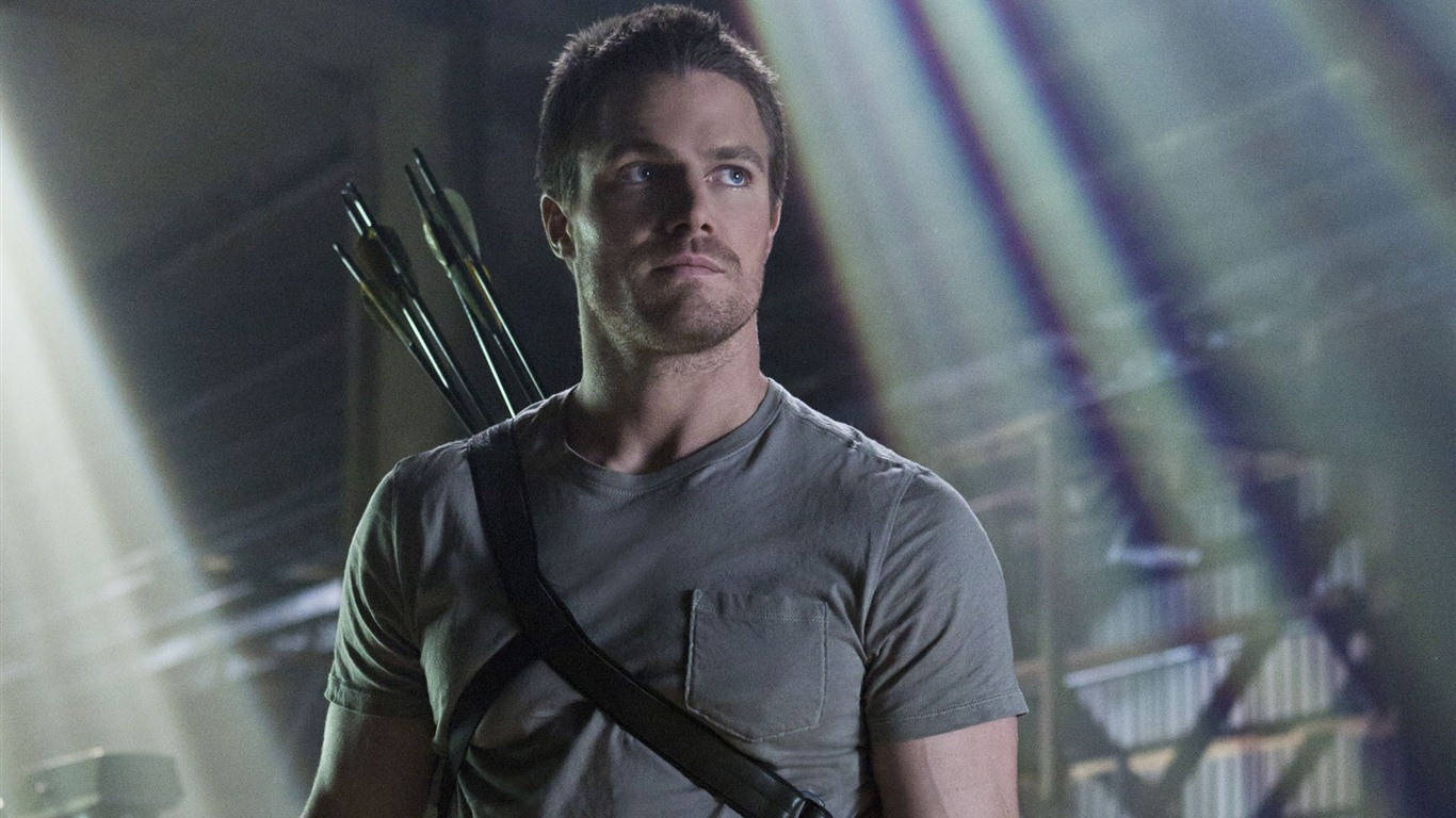 Green Arrow 桌布 壁紙 — 一個背上插著箭的男人站在光線昏暗的工業空間中，戲劇性的光束穿過煙霧。