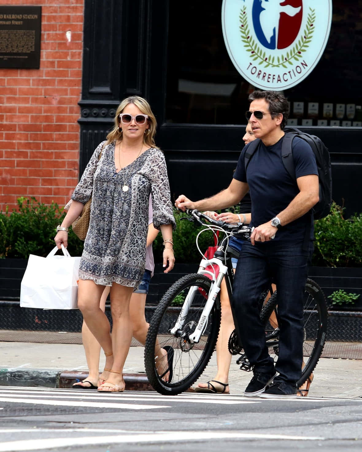 Christine Taylor 桌布 壁紙 — 一個背著背包的男人推著腳踏車，旁邊一個女人拿著白色購物袋，在城市的行人道上行走。