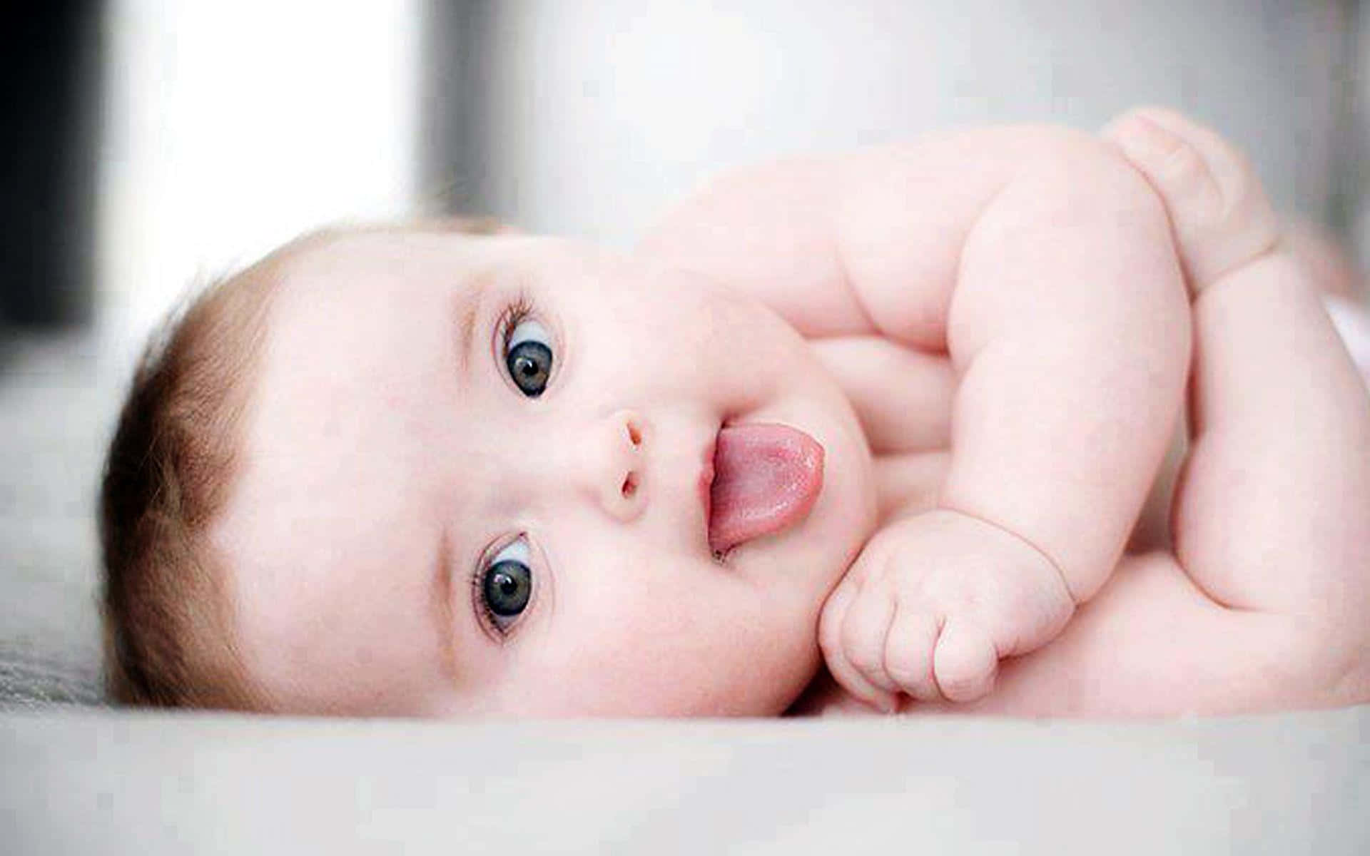 cute baby 桌布 壁紙 — 一個胖嘟嘟的寶寶，有著大大的藍眼睛，仰臥著頑皮地伸出舌頭。