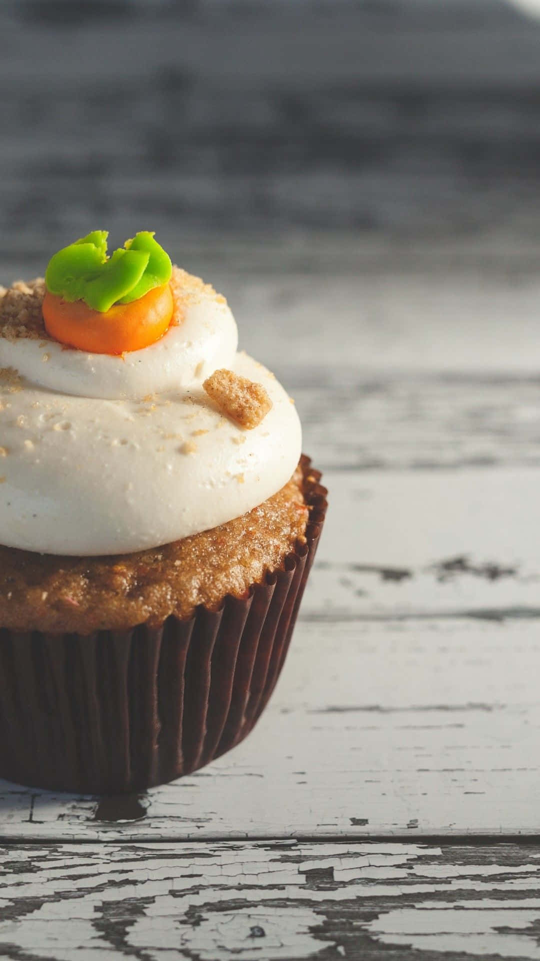 Cupcake 桌布 壁紙 — 一個胡蘿蔔蛋糕杯子蛋糕，上面有白色糖霜和胡蘿蔔裝飾，放在一個風化的白色木質表面上。