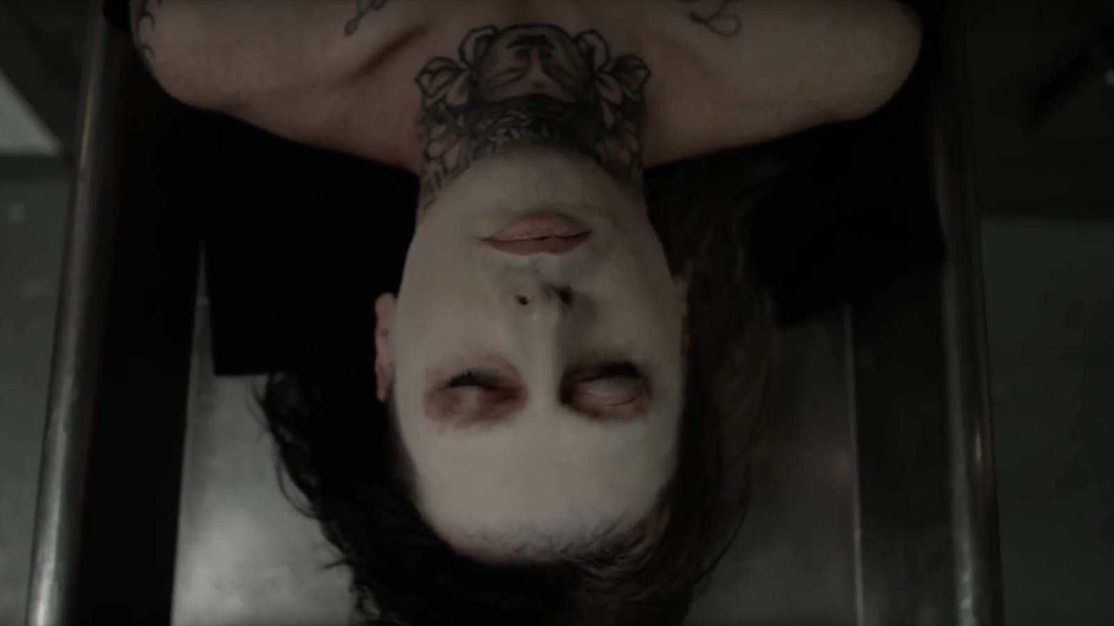 Ghostemane 桌布 壁紙 — 一個臉上塗有白色顏料、頸部有刺青的人，倒掛在一個金屬棺材狀的結構中。