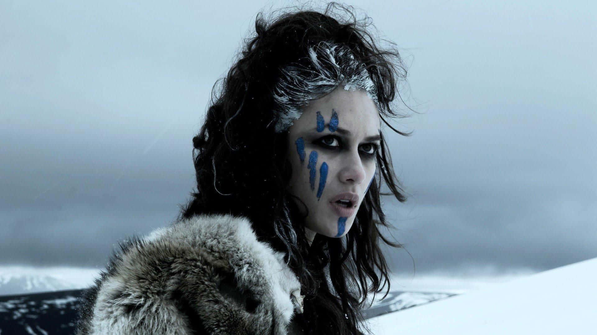 Olga Kurylenko 桌布 壁紙 — 一個臉上塗著藍色顏料、頭髮結霜的兇猛女人，穿著毛皮襯裡大衣，站在雪地荒野中。