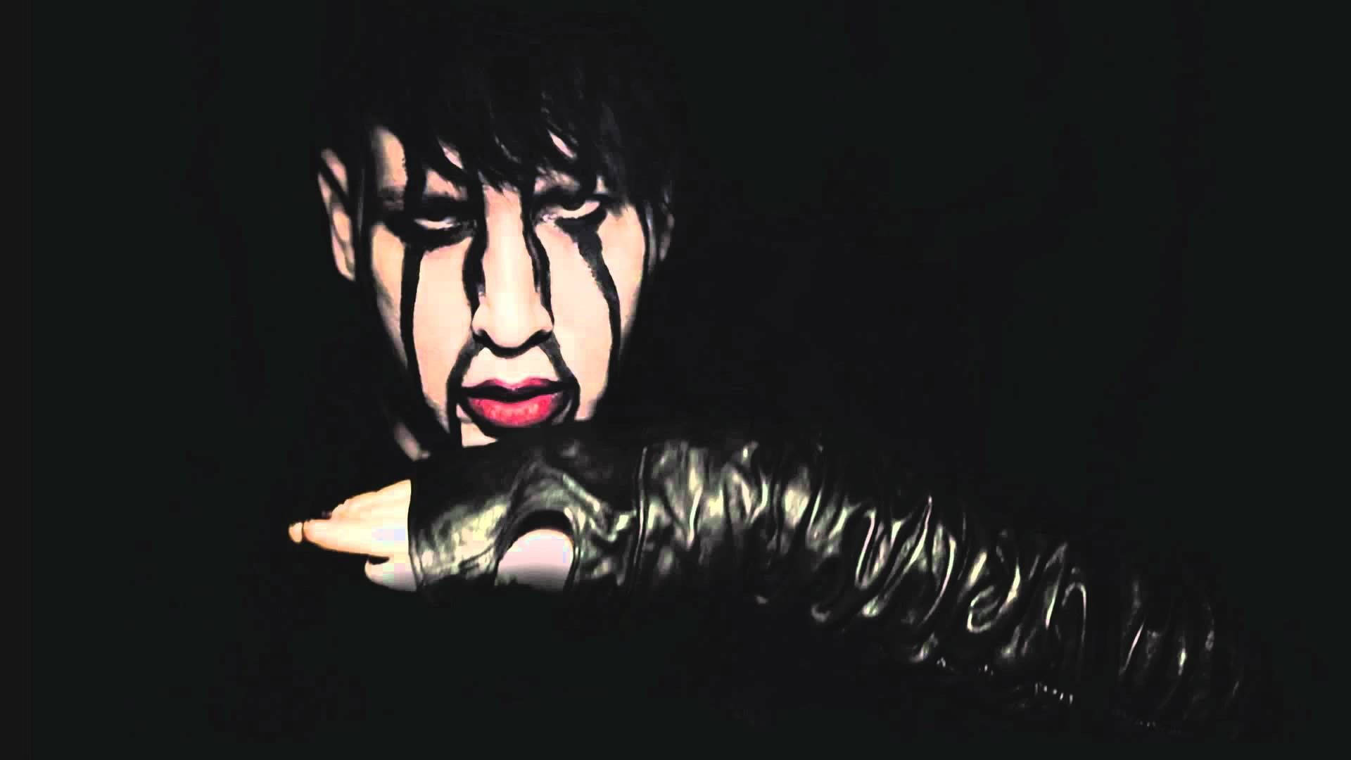 marilyn manson 桌布 壁紙 — 一個臉上畫著戲劇性黑色顏料和紅唇的人，在黑暗背景中伸出一隻戴著手套的手。