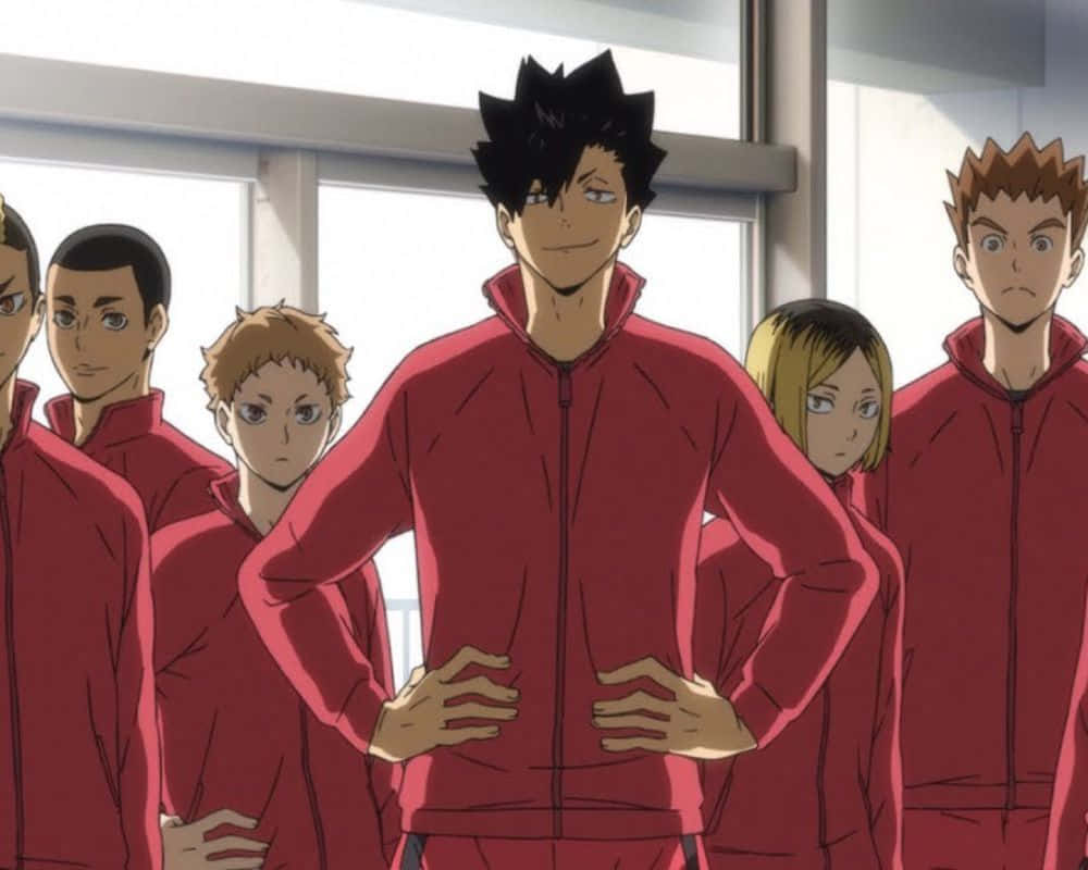 Haikyuu Nekoma 桌布 壁紙 — 一個自信的動漫排球運動員穿著紅色運動服，雙手叉腰站立，兩旁是隊友，背景是明亮的體育館。