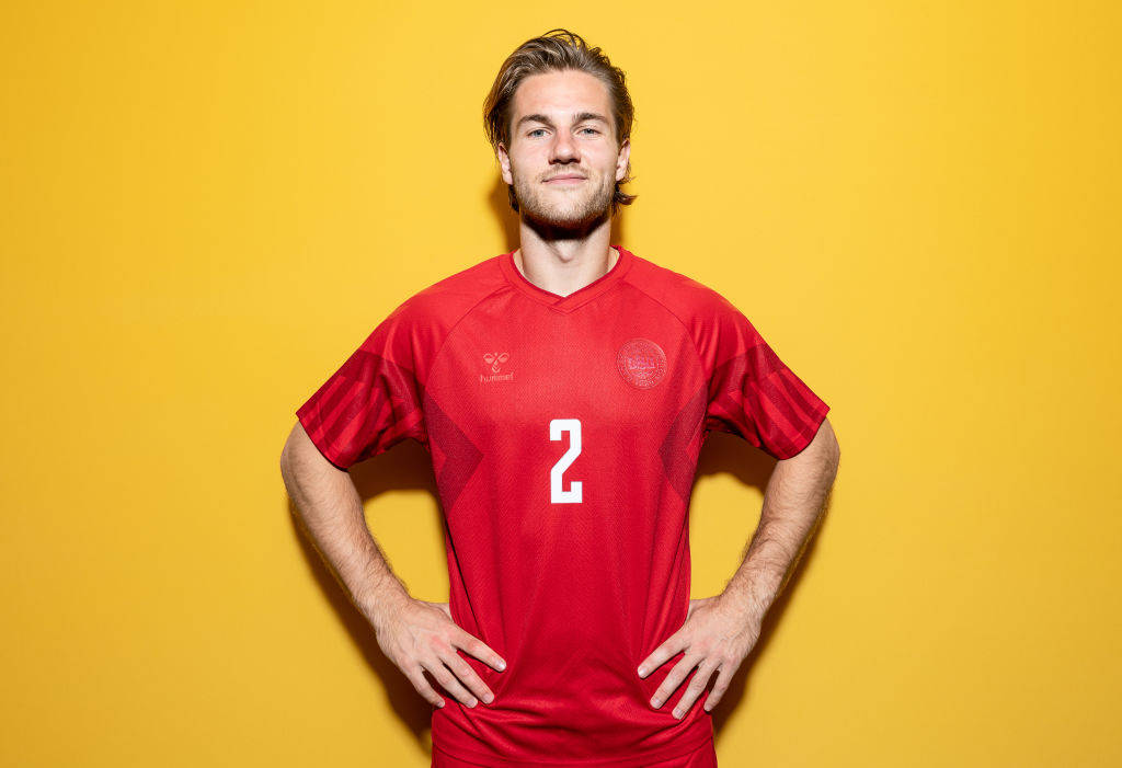 Football Players 桌布 壁紙 — 一個自信的年輕足球員，身穿紅色球衣，背號二號，站在鮮黃色背景前。