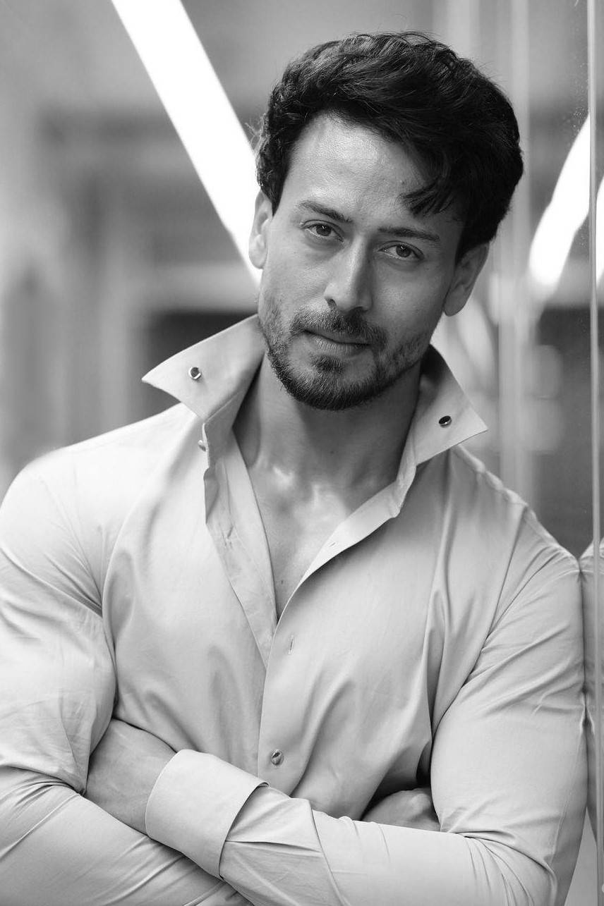 Tiger Shroff 桌布 壁紙 — 一個自信的男人，深色頭髮和鬍鬚，站在黑白肖像中，雙臂交叉，表情嚴肅。