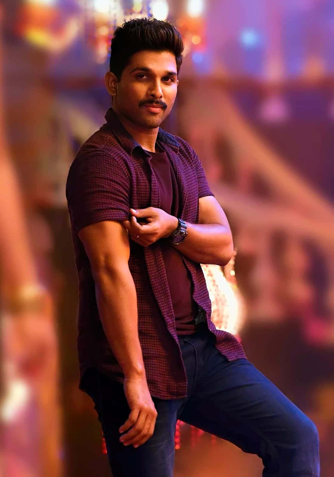Allu Arjun 桌布 壁紙 — 一個自信的男人穿著栗色格紋襯衫，一手放在手臂上，在充滿活力的模糊舞台背景前擺姿勢。