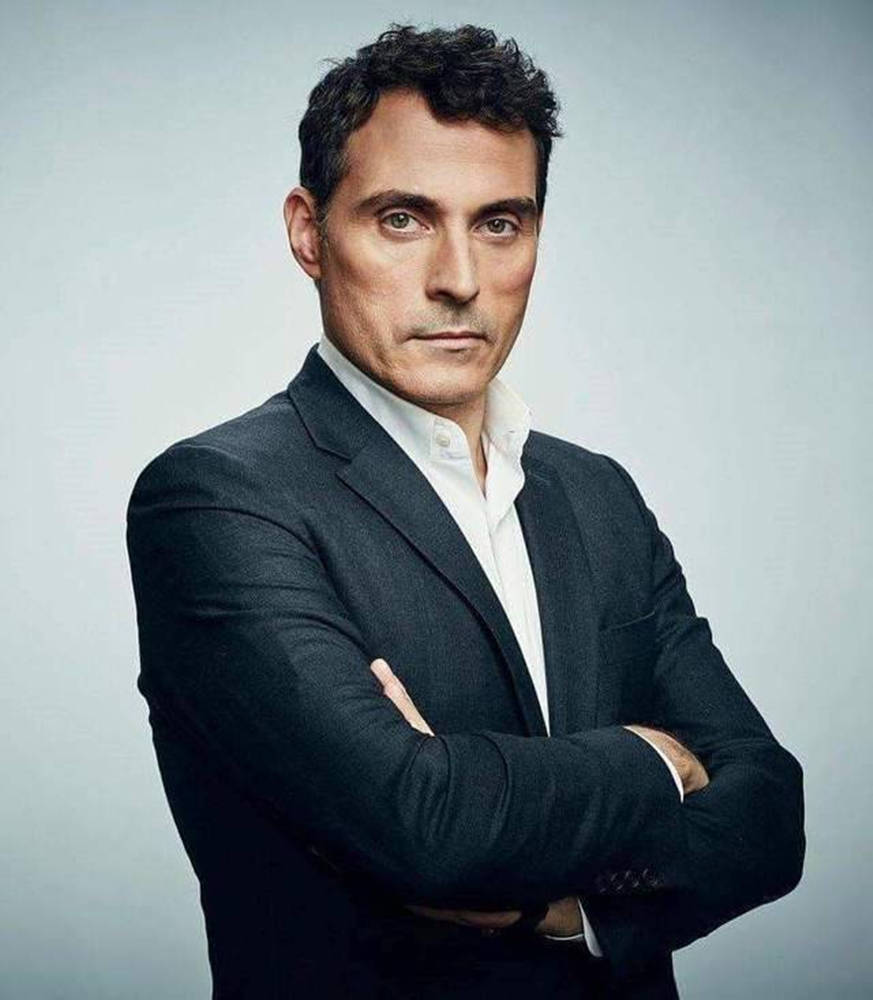actor 桌布 壁紙 — 一個自信的男人穿著深色西裝，雙手交叉站在純灰色背景前，散發出權威和冷靜的強烈氣場。