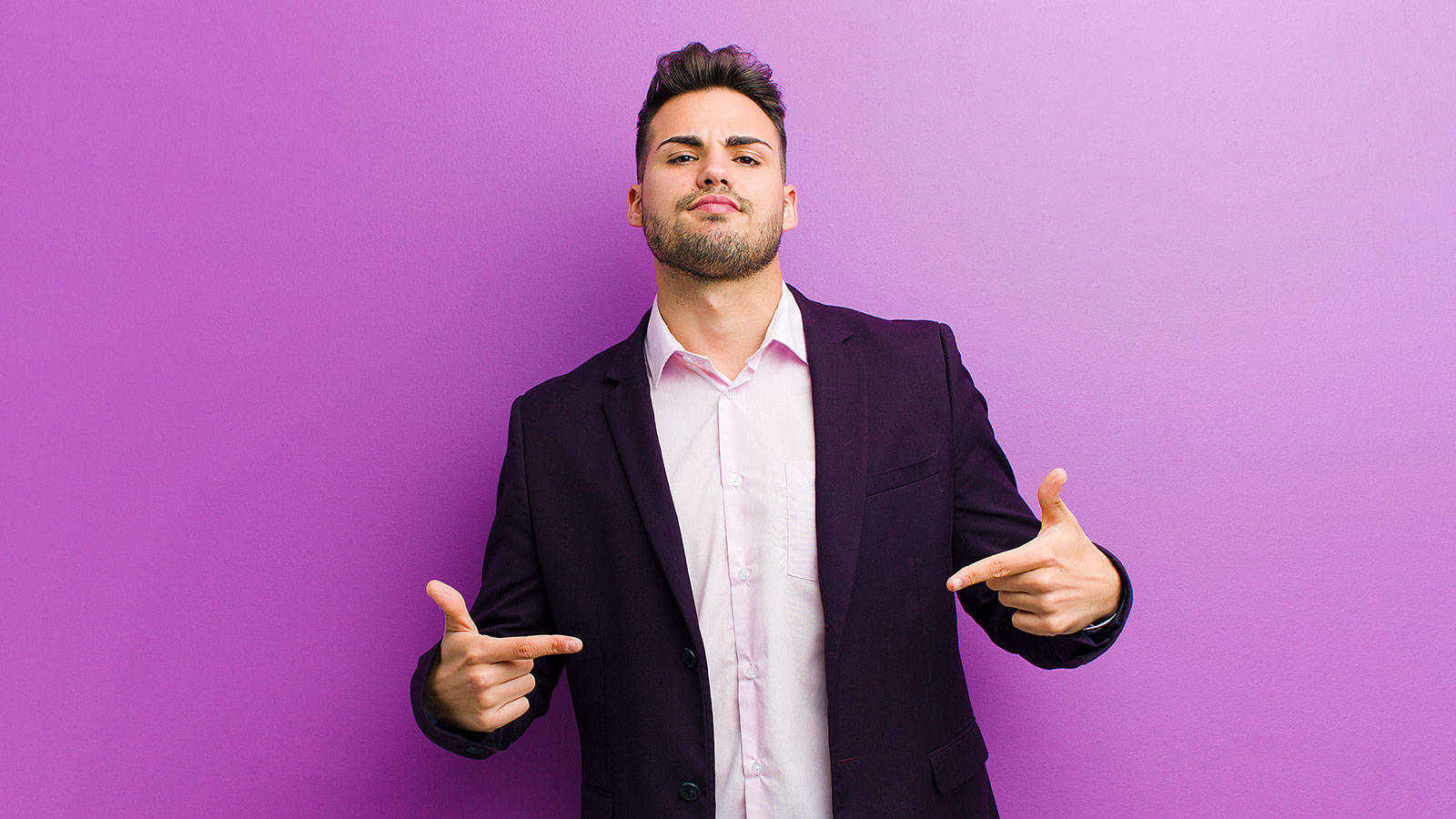 Winner 桌布 壁紙 — 一個自信的男人穿著深色西裝和粉紅色襯衫，在純紫色背景前指著自己。