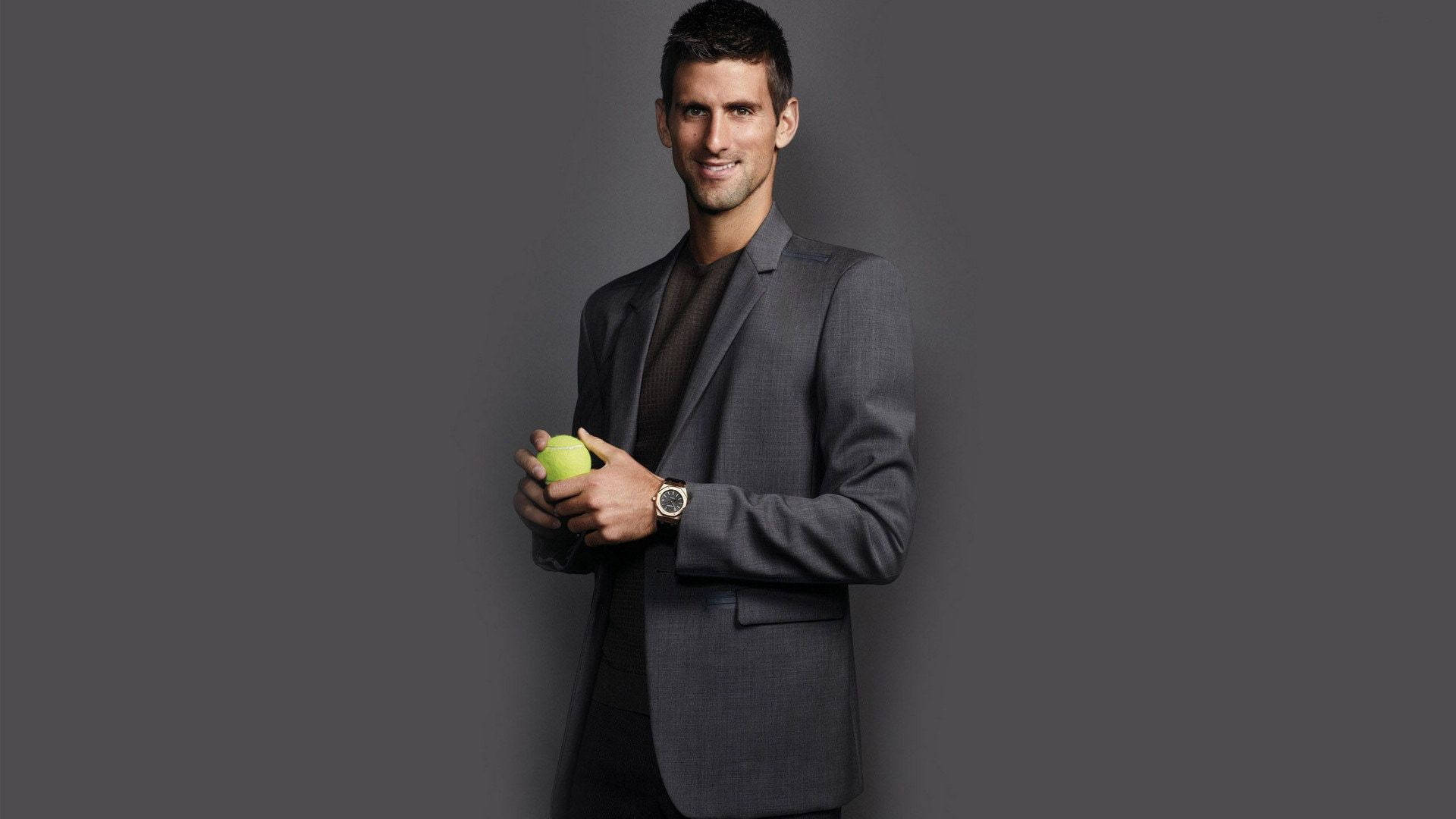 Novak 桌布 壁紙 — 一個自信的男人穿著灰色西裝，在純深灰色的攝影棚背景前拿著一個亮綠色的網球。