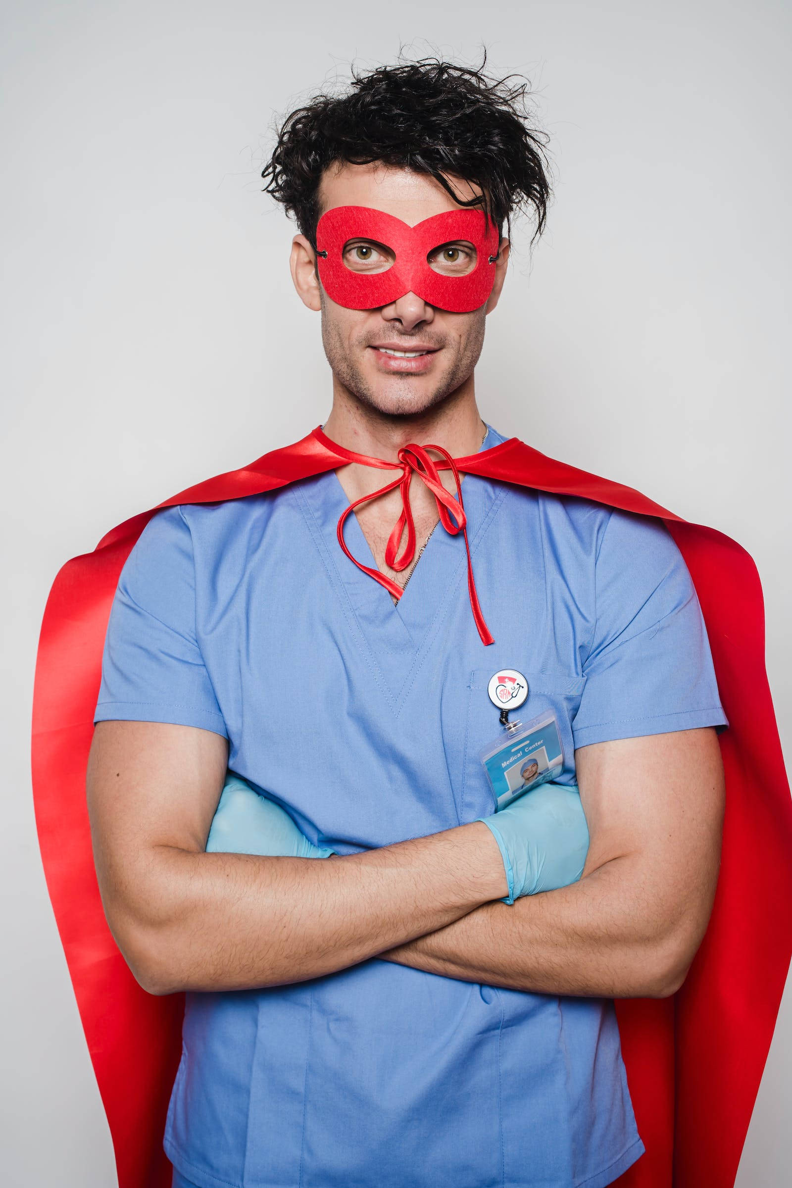 doctor motivation 桌布 壁紙 — 一個自信的男人穿著藍色手術服和紅色超級英雄面具，在簡單背景前交叉雙臂站立。