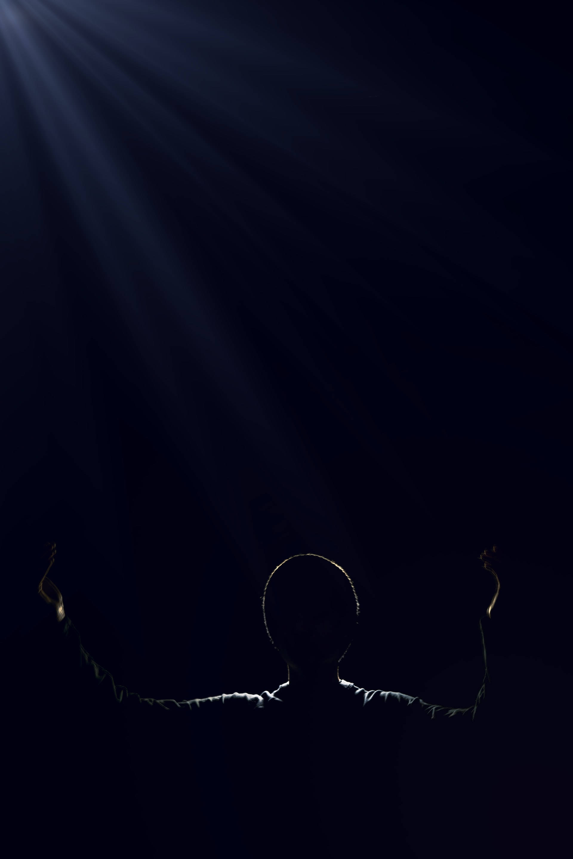 Silhouette 桌布 壁紙 — 一個舉起雙臂的剪影人物站在黑暗中，神聖的光芒從上方照射下來。