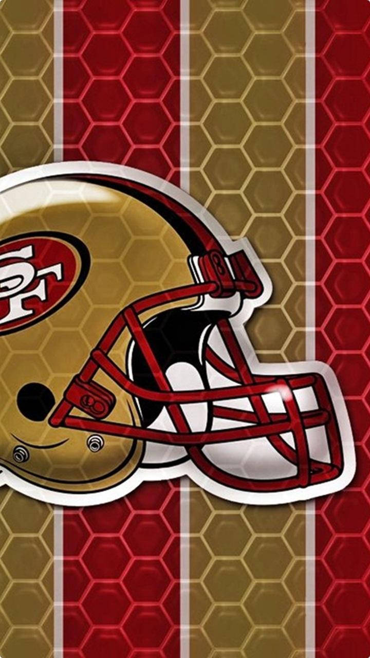 49ers 桌布 壁紙 — 一個舊金山49人隊的金色和紅色美式足球頭盔放置在六角形圖案和垂直條紋的背景上。