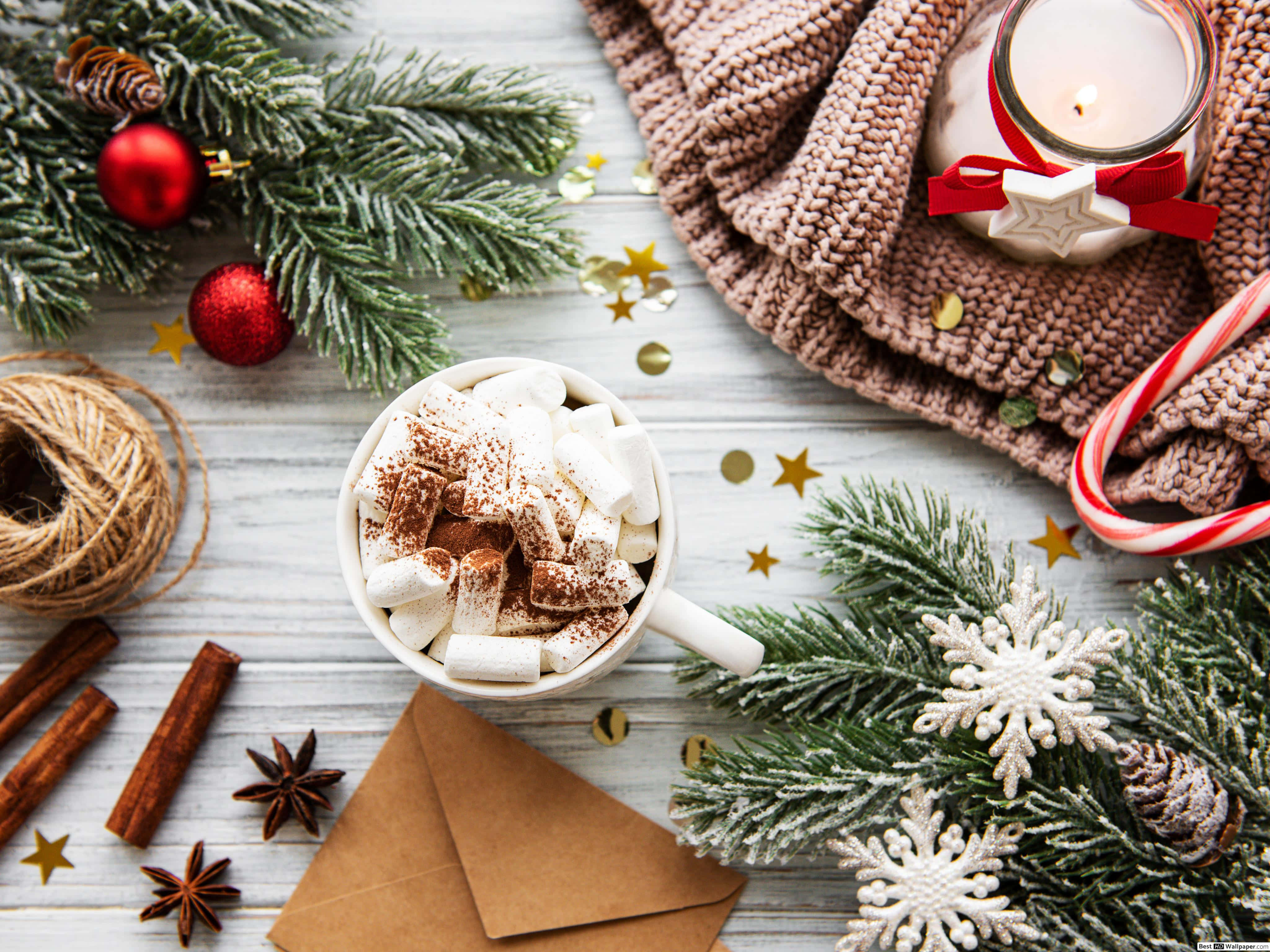 Hot Chocolate 桌布 壁紙 — 一個舒適的冬季場景，一杯熱可可上面放著棉花糖和肉桂，周圍環繞著松樹枝、拐杖糖和點燃的蠟燭。