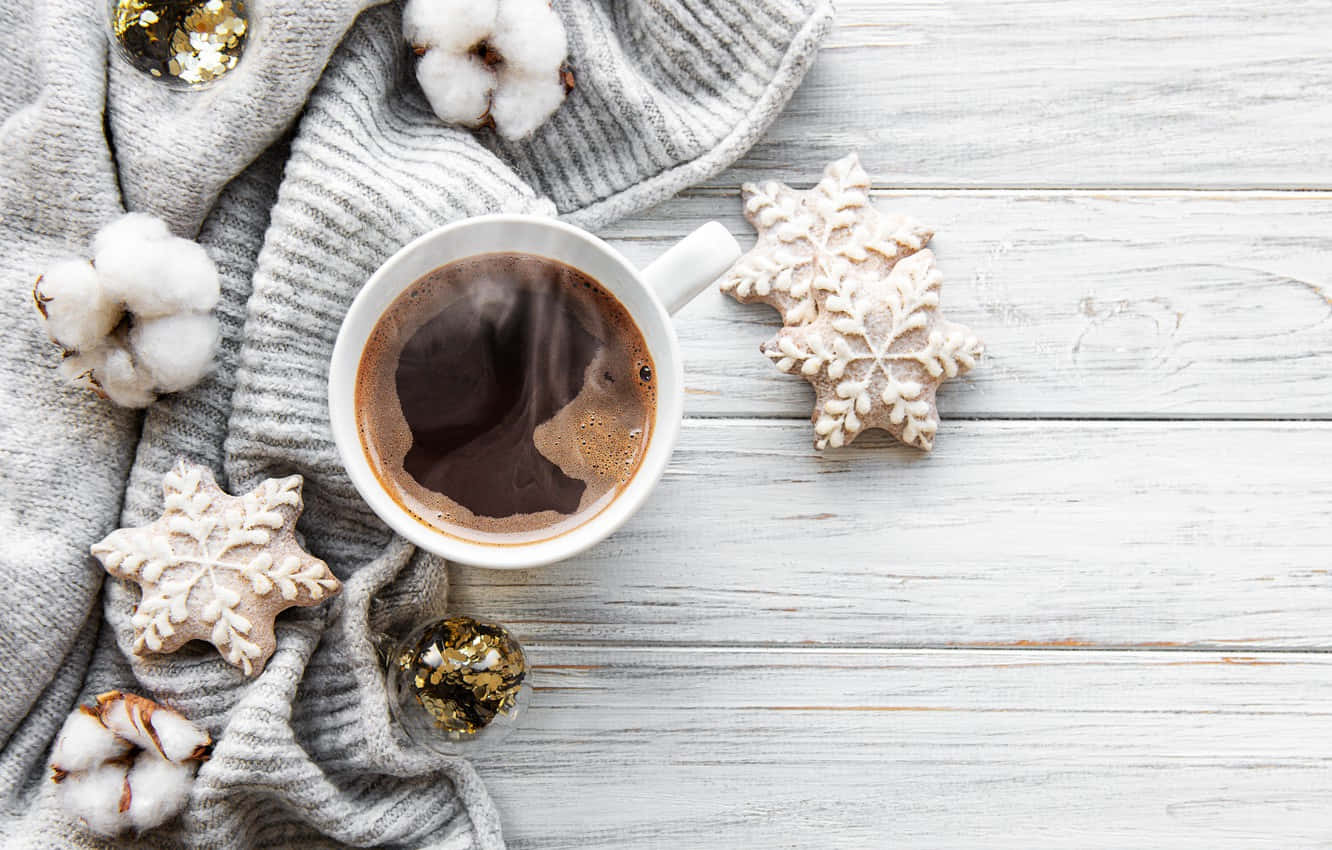 Cozy Winter Desktop 桌布 壁紙 — 一個舒適的冬日場景，一杯冒著熱氣的咖啡，周圍有雪花餅乾、棉鈴和一條柔軟的灰色針織圍巾，放在白色的木質表面上。