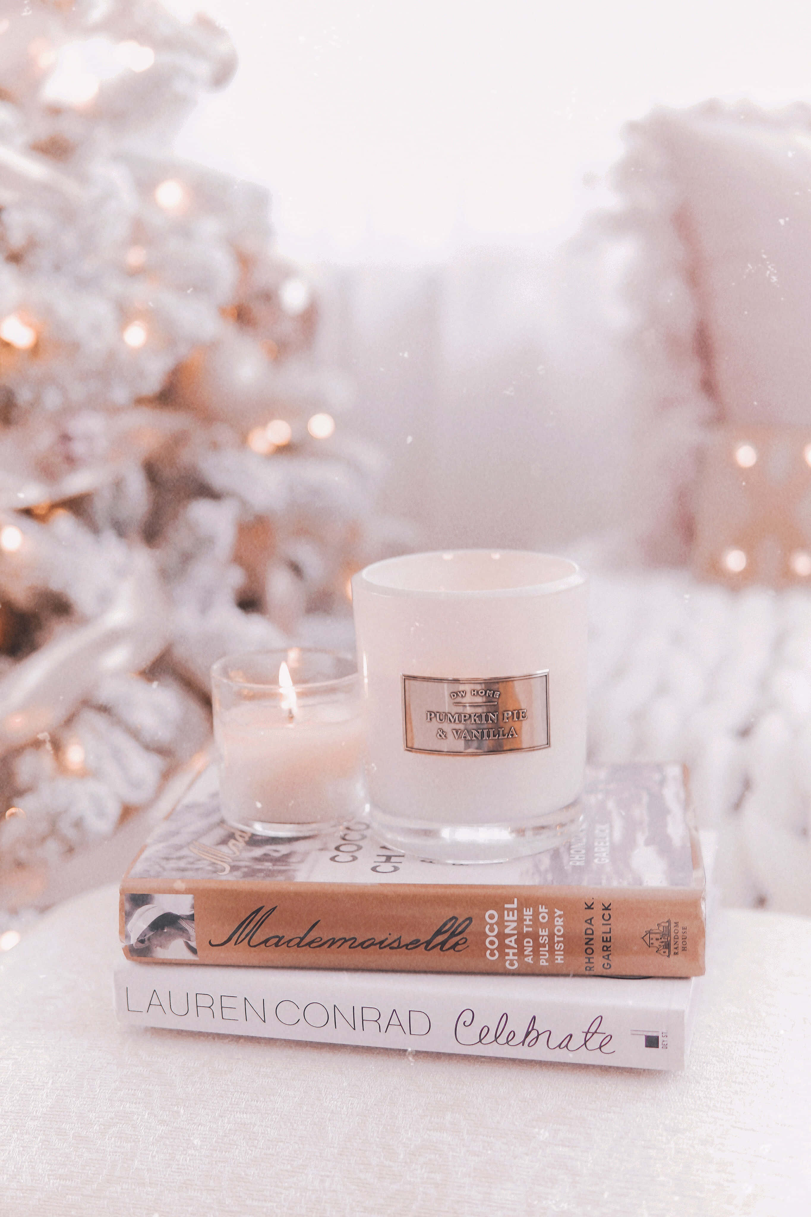 Rose Gold Christmas 桌布 壁紙 — 一個舒適的冬日場景，點燃的蠟燭放在書本上，旁邊是一棵裝飾著溫暖仙女燈的雪樹。