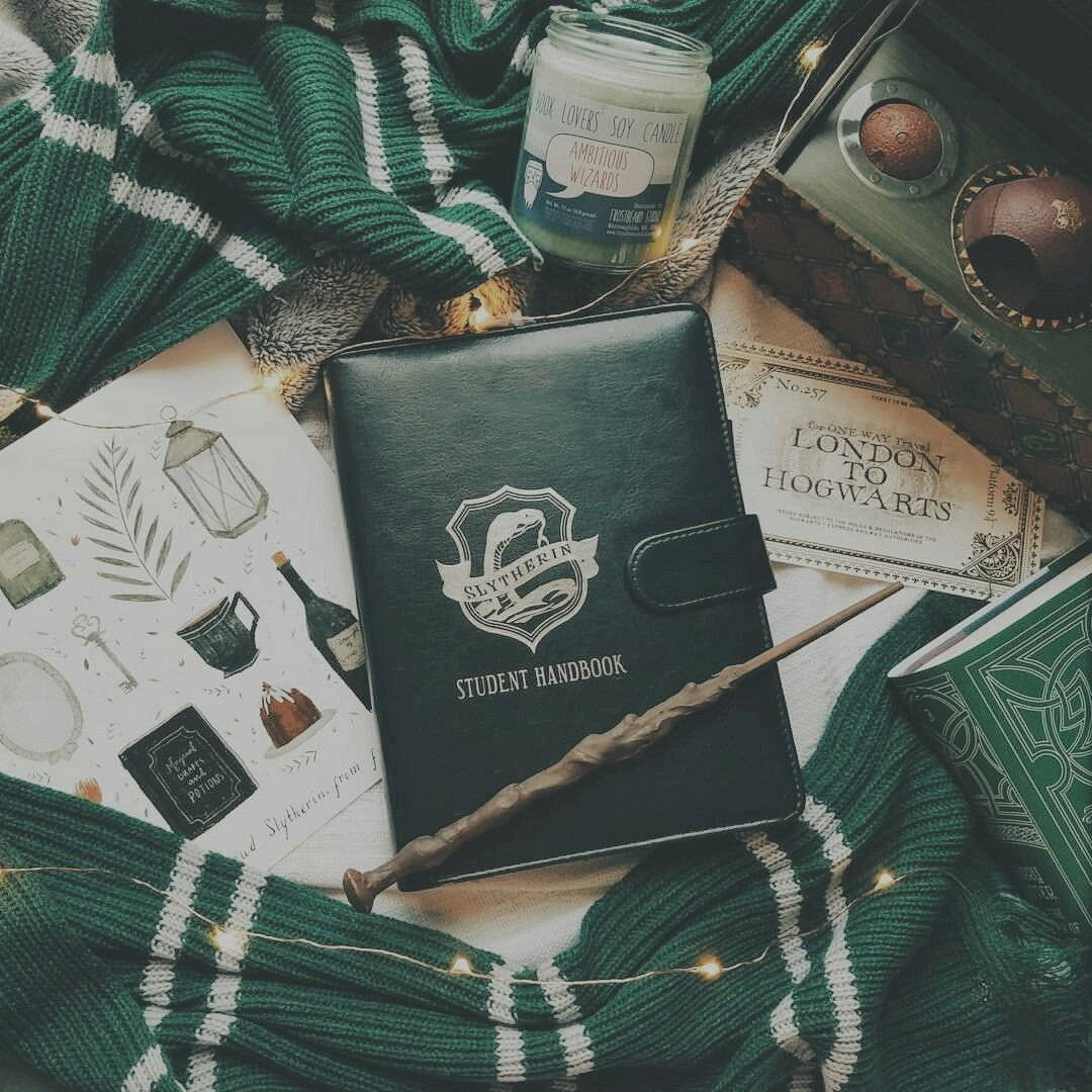 hp aesthetic 桌布 壁紙 — 一個舒適的史萊哲林主題平面佈置，包含綠色條紋圍巾、學生手冊、魔杖、蠟燭和魔法文具。