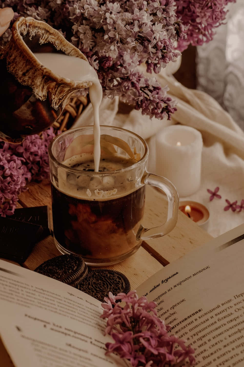Floral Tea 桌布 壁紙 — 一個舒適的場景，牛奶倒入咖啡中，旁邊有丁香、巧克力餅乾和點燃的蠟燭在木桌上。