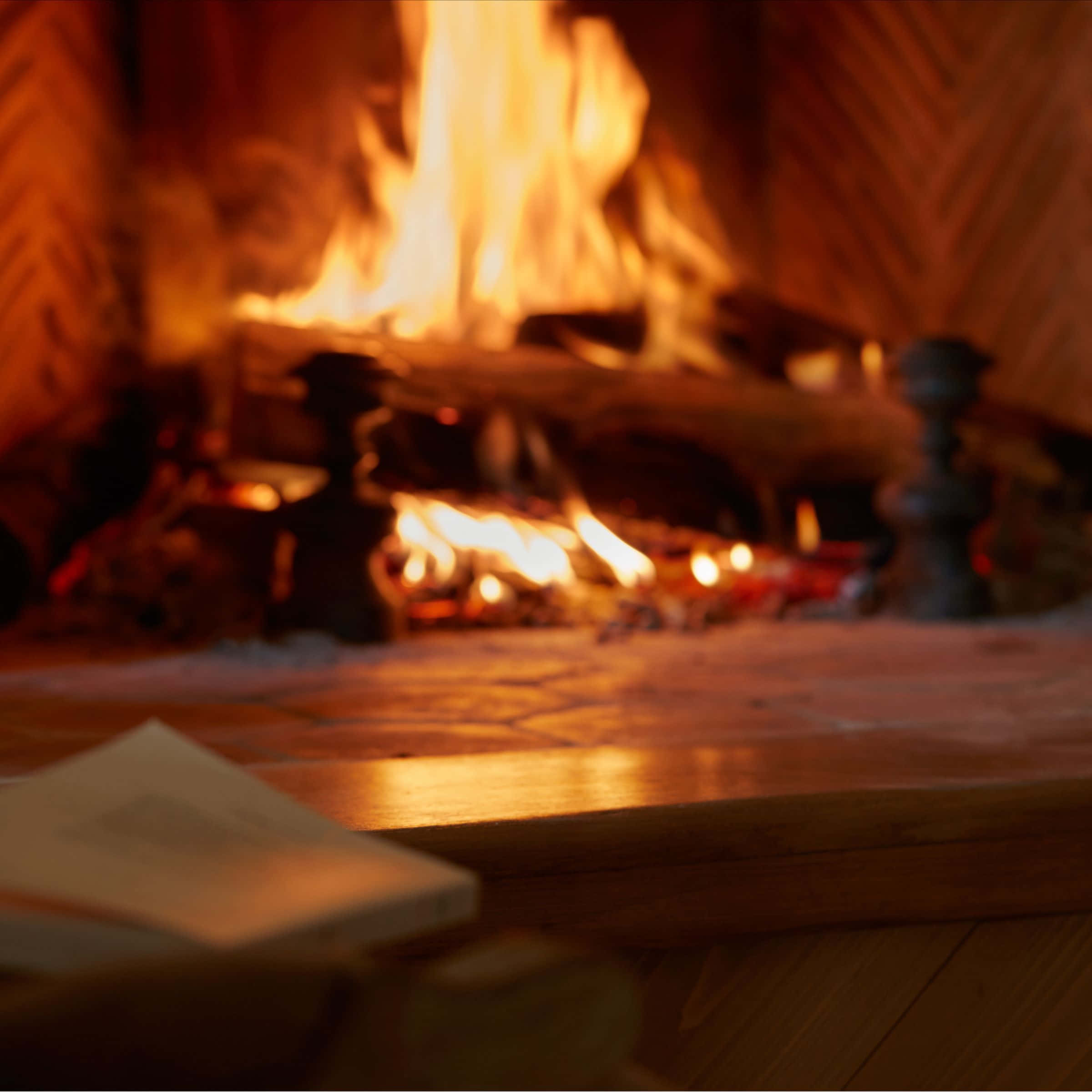 Cozy Fire 桌布 壁紙 — 一個舒適的壁爐，劈啪作響的火焰在木製壁爐架和地板上投射出溫暖的金色光芒。
