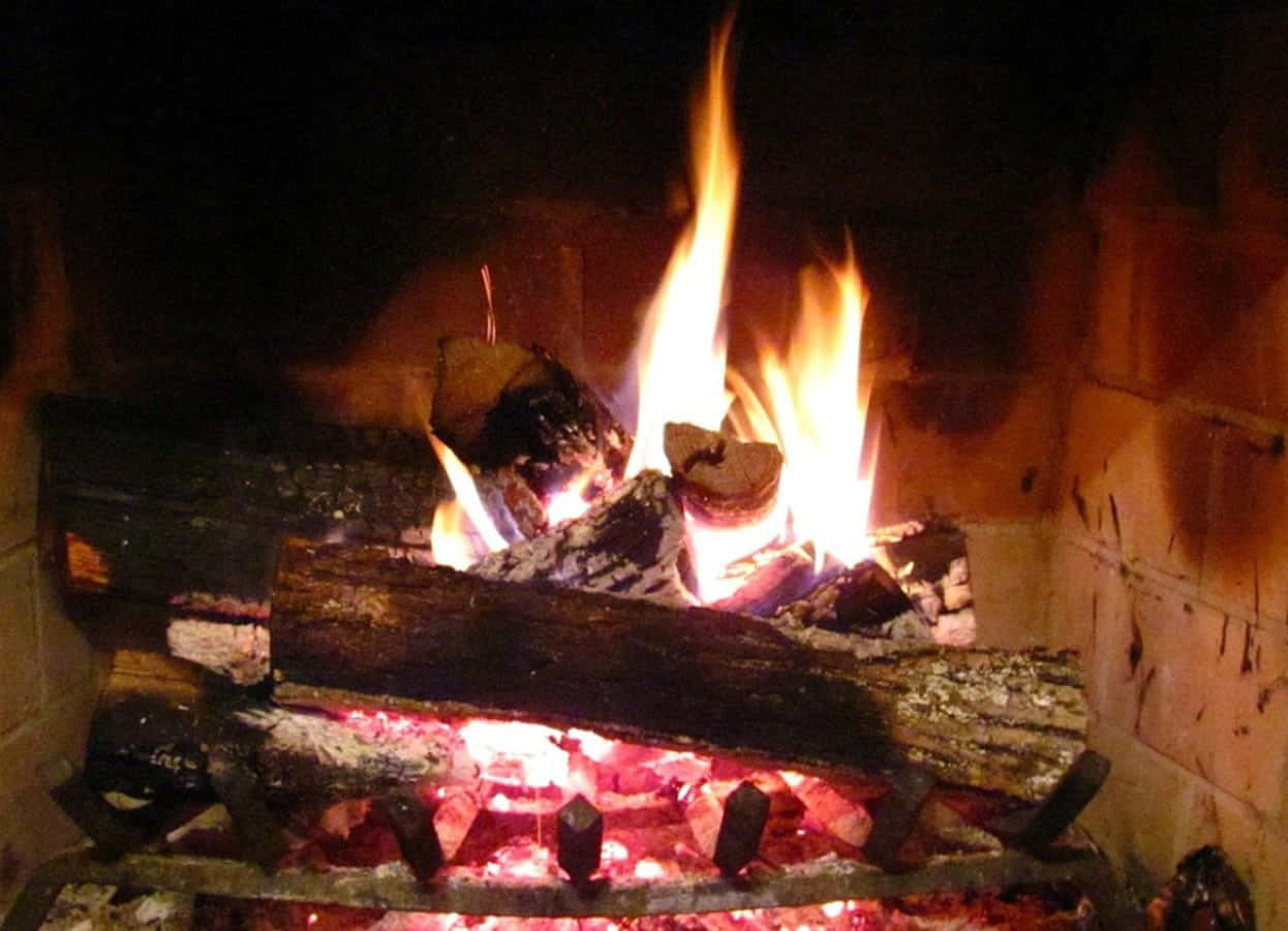 Autumn Fireplace 桌布 壁紙 — 一個舒適的壁爐在昏暗的房間裡，對著深色磚牆發出噼啪聲，燃燒著鮮豔的橙色火焰和發光的餘燼。