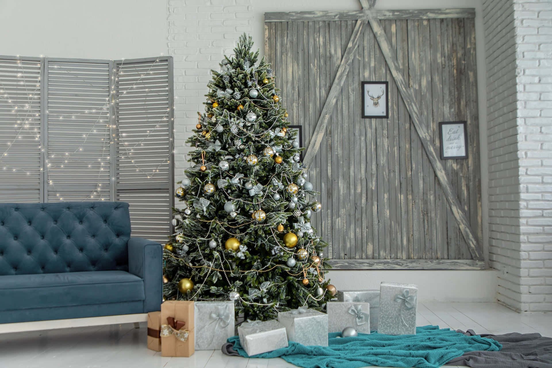 Aesthetic Christmas Tree 桌布 壁紙 — 一個舒適的客廳，裝飾著金色和銀色飾品的聖誕樹，旁邊是一張藍色簇絨沙發和質樸的木門。
