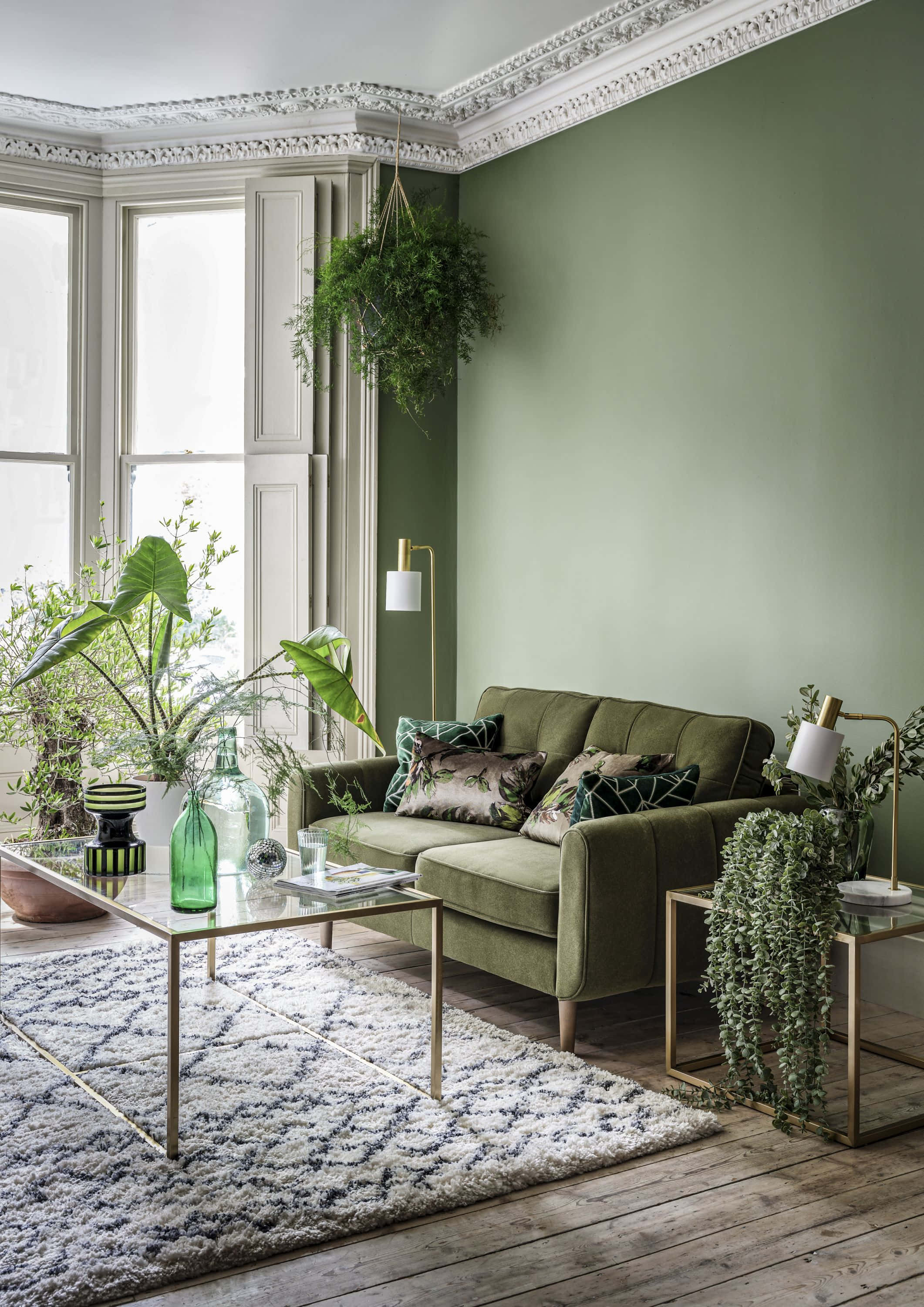 Living Room 桌布 壁紙 — 一個舒適的客廳，配有綠色天鵝絨沙發、木地板，以及大量懸掛和盆栽植物，沐浴在自然光中。