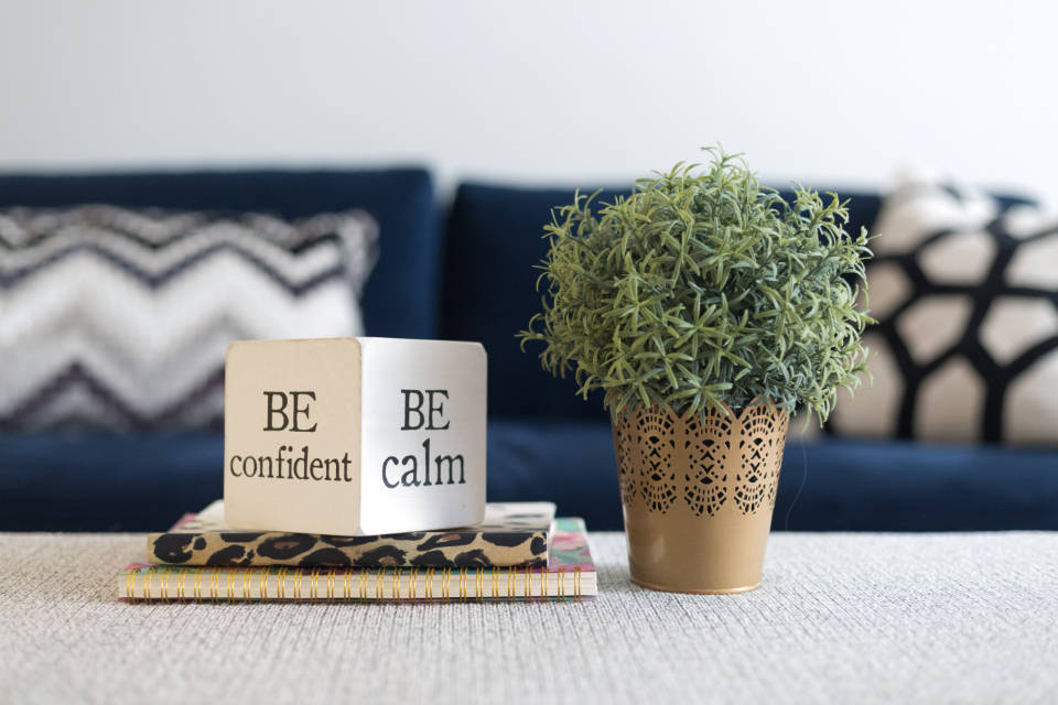 勵志桌面 桌布 壁紙 — 一個舒適的客廳場景，木塊上寫著「BE confident BE calm」，旁邊有一盆綠色植物放在有紋理的桌子上。