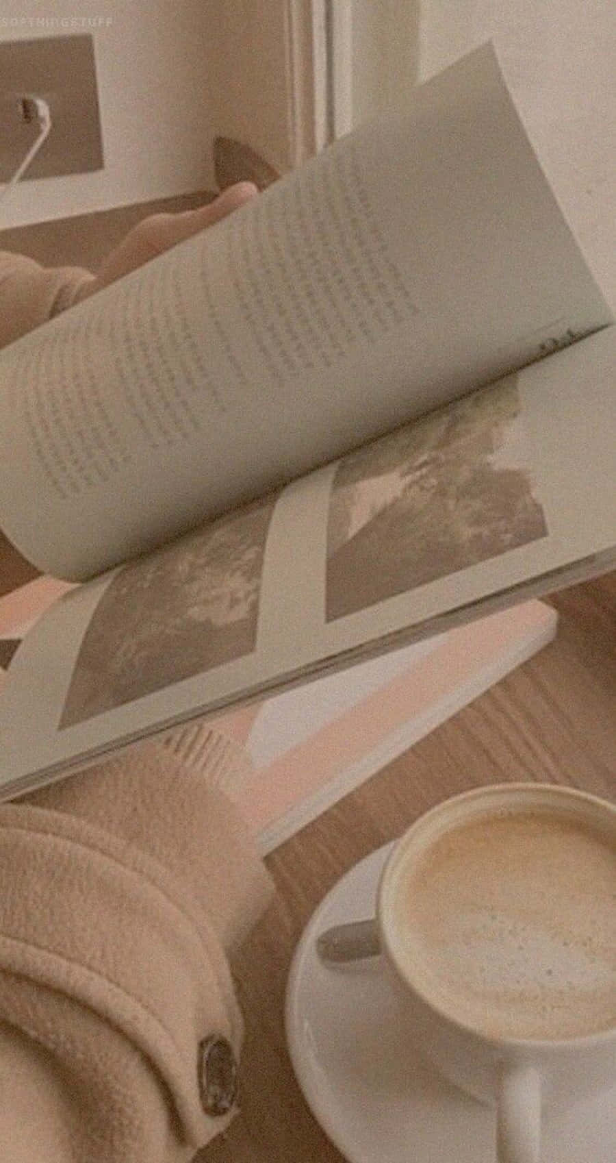 Korean Beige Aesthetic 桌布 壁紙 — 一個舒適的室內場景，雙手捧著一本打開的書，旁邊是一杯冒著熱氣的咖啡，放在木桌上。