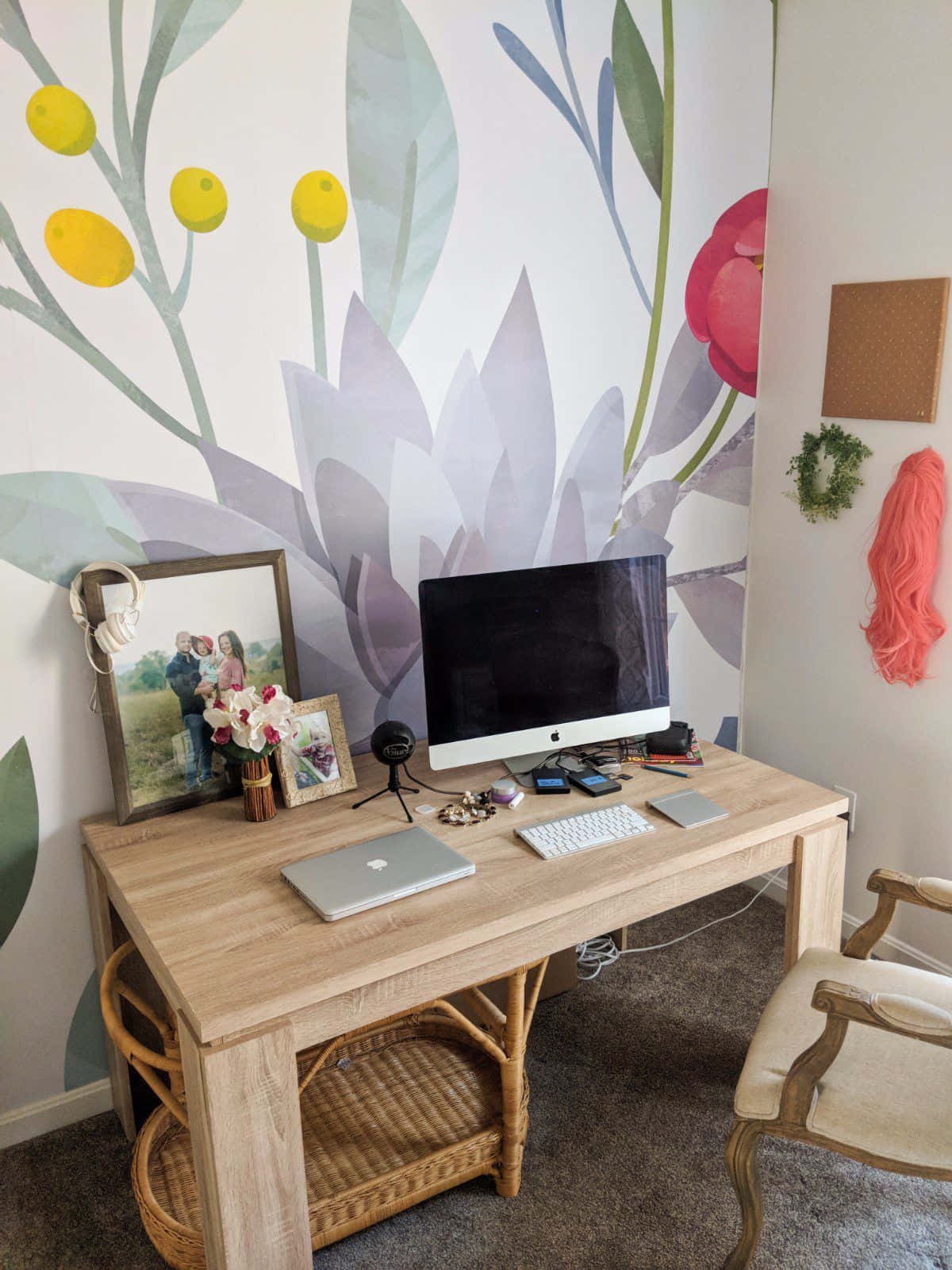 Working From Home 桌布 壁紙 — 一個舒適的家庭辦公室，木製書桌對著充滿活力的花卉壁紙，上面有大型紫色花朵和黃色漿果。