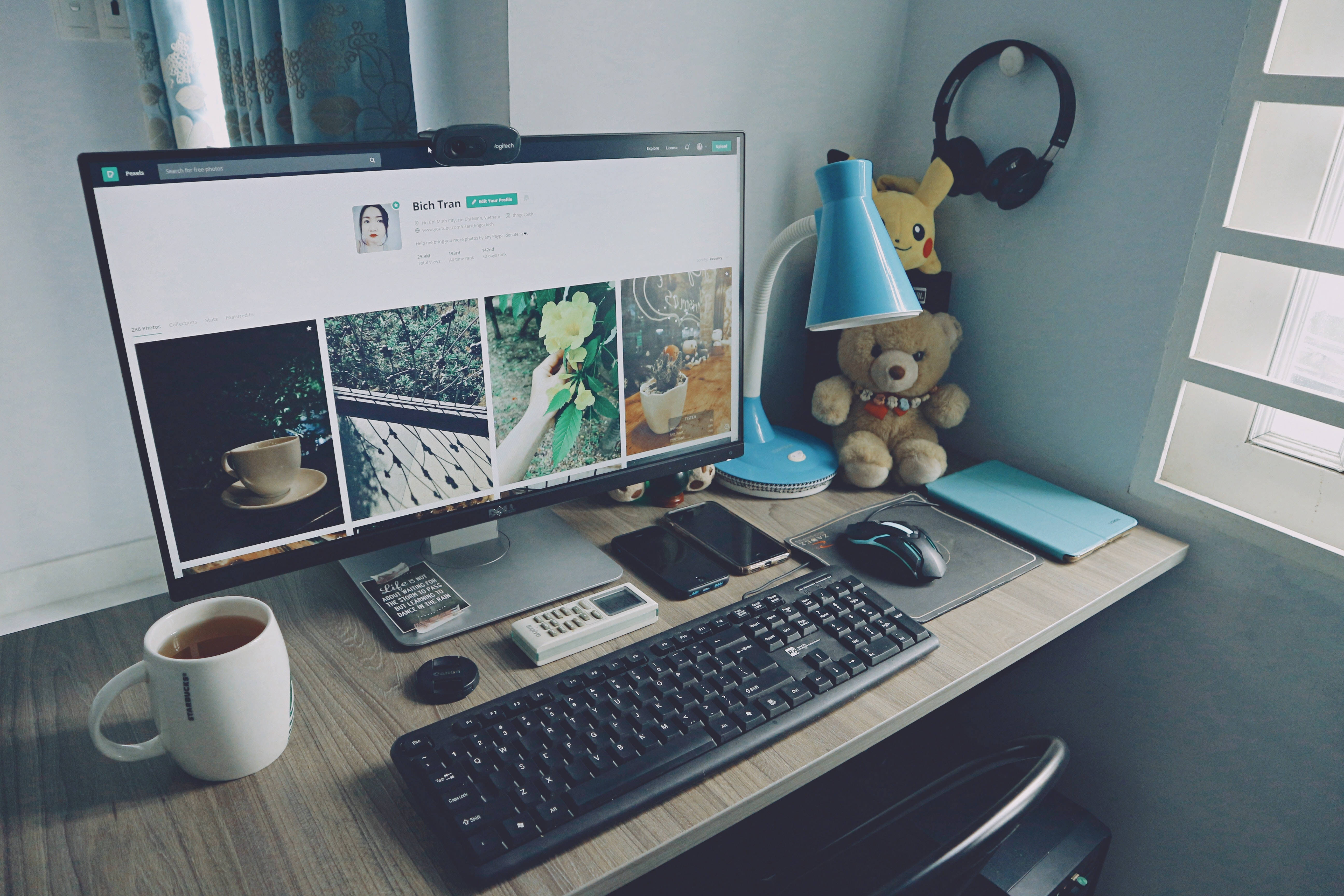 Desk 桌布 壁紙 — 一個舒適的家庭辦公室書桌，配有顯示照片的電腦顯示器、一杯茶、一隻泰迪熊和一盞藍色燈。