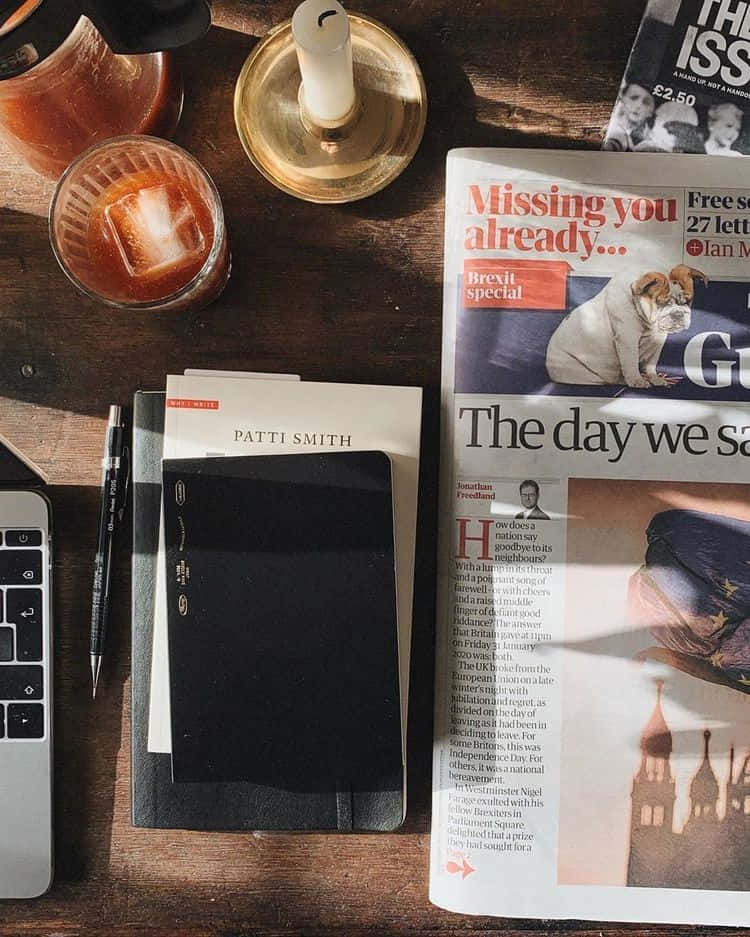 Studying 桌布 壁紙 — 一個舒適的書桌場景，有報紙Brexit特刊、雞尾酒、蠟燭、筆記本和筆記型電腦，沐浴在溫暖的陽光中。