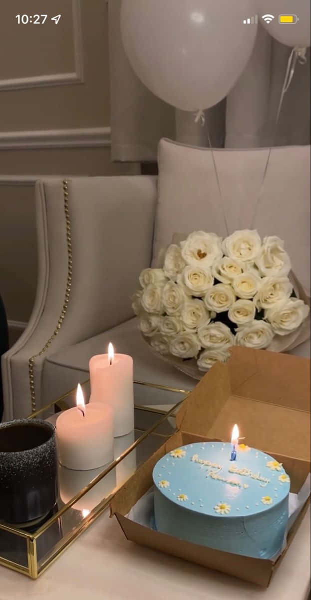 Birthday Message 桌布 壁紙 — 一個舒適的生日佈置，有藍色蛋糕、一支蠟燭、白玫瑰和氣球，放在鏡面托盤上，旁邊是沙發。