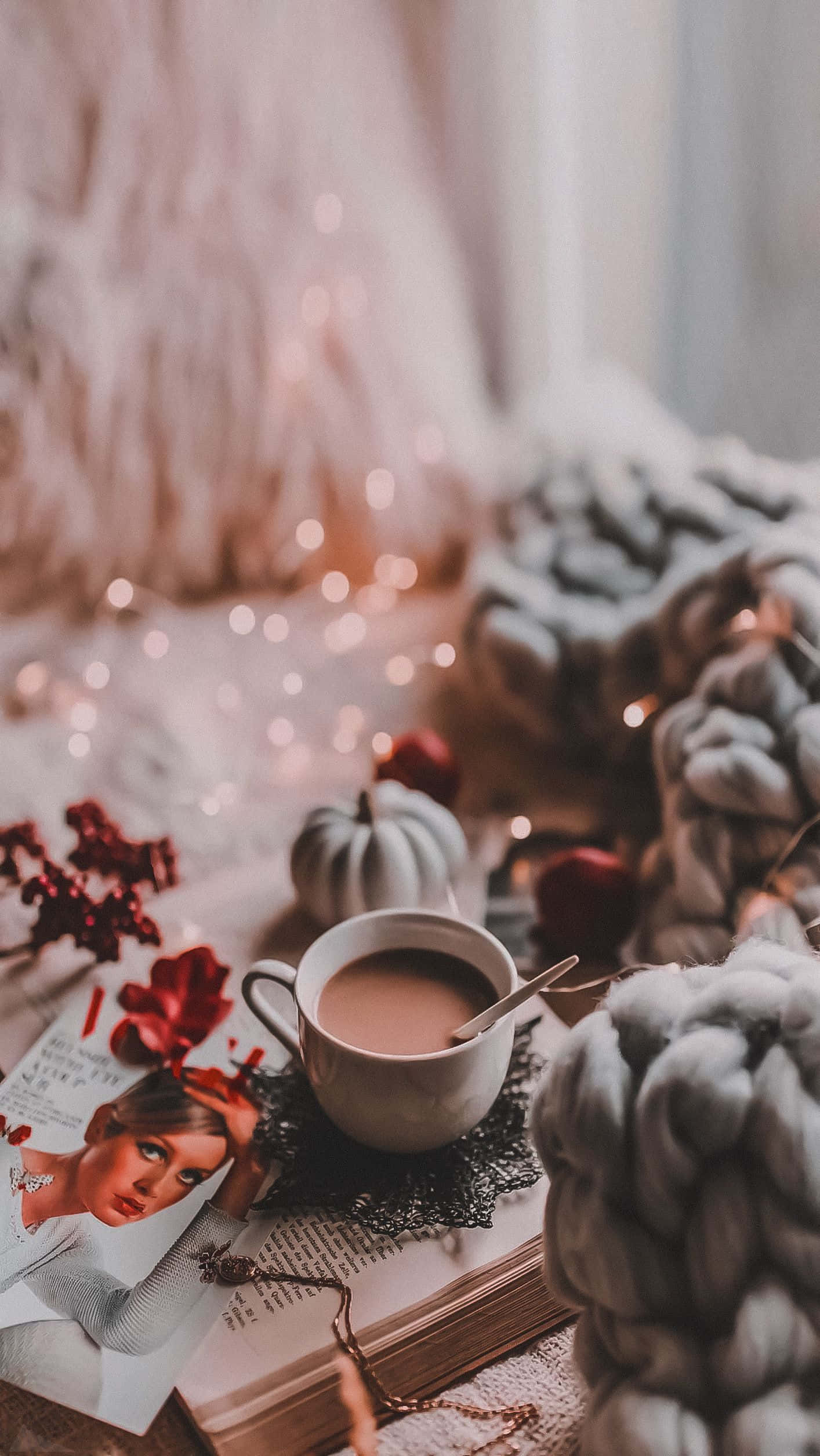 Cozy iPhone 桌布 壁紙 — 一個舒適的秋日場景，一杯冒著熱氣的咖啡放在打開的書本上，周圍是針織毯子和閃爍的仙女燈。