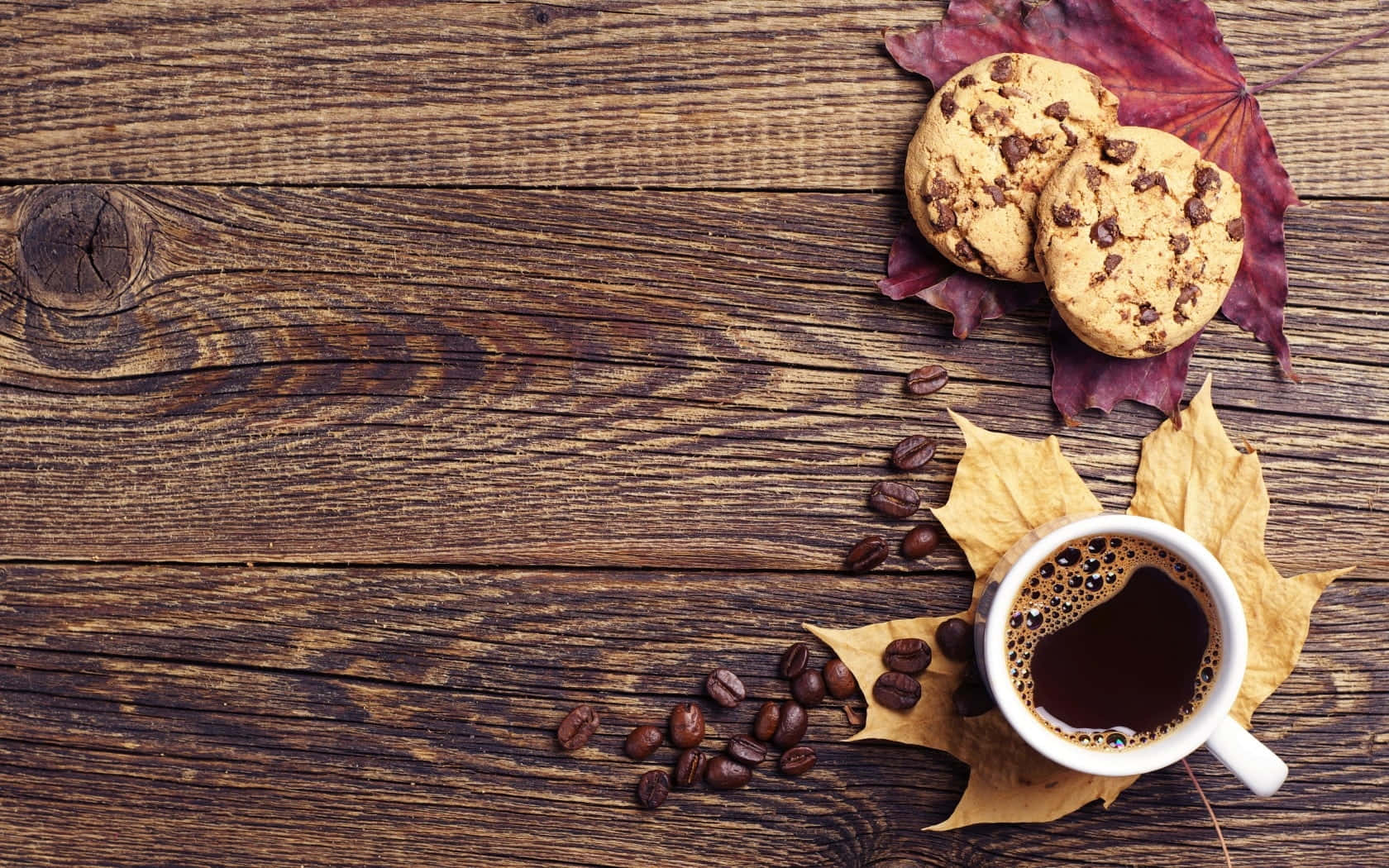 Autumn Food 桌布 壁紙 — 一個舒適的秋日場景，一杯冒著熱氣的咖啡、巧克力餅乾和散落的咖啡豆，放在裝飾著鮮豔秋葉的質樸木板上。