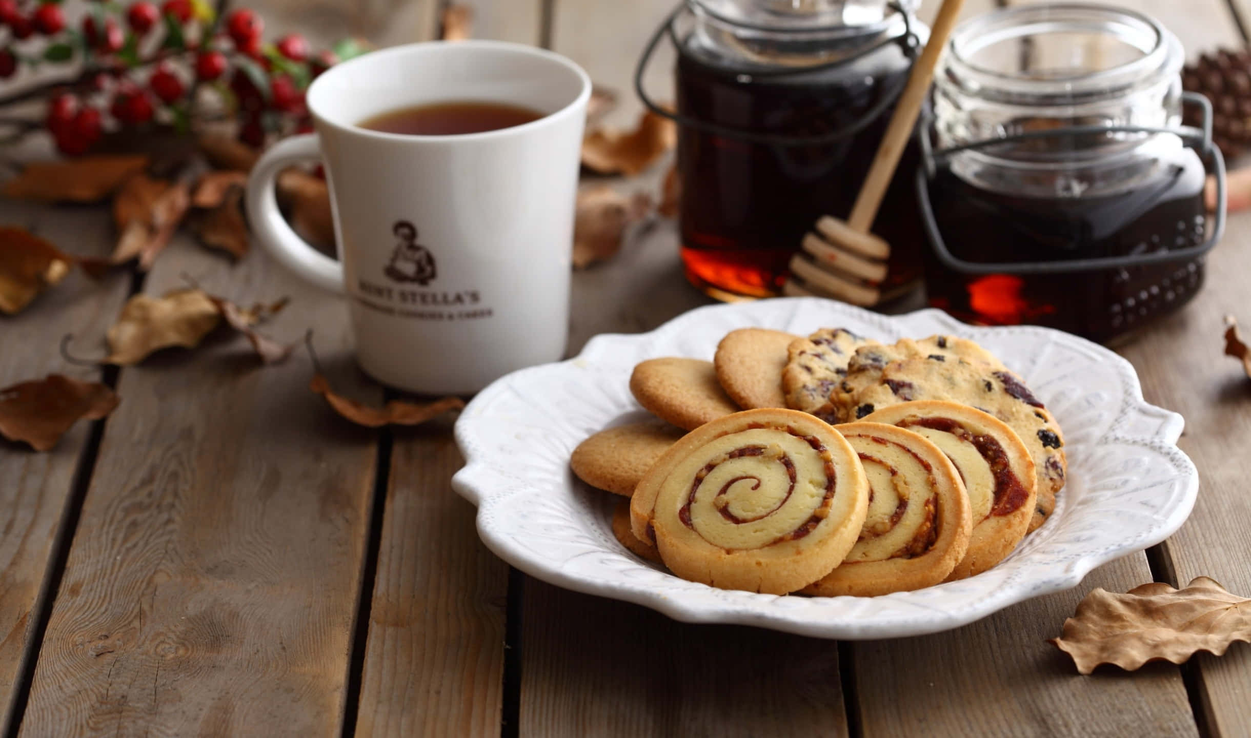Cookies 桌布 壁紙 — 一個舒適的秋日場景，木桌上放有蜂蜜漩渦餅乾、一杯茶和蜂蜜罐，周圍散落著落葉。