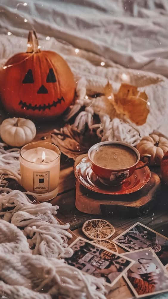 Fall Halloween iPhone 桌布 壁紙 — 一個舒適的秋日場景，木桌上鋪著白色針織布，上面有雕刻南瓜蠟燭和咖啡杯。