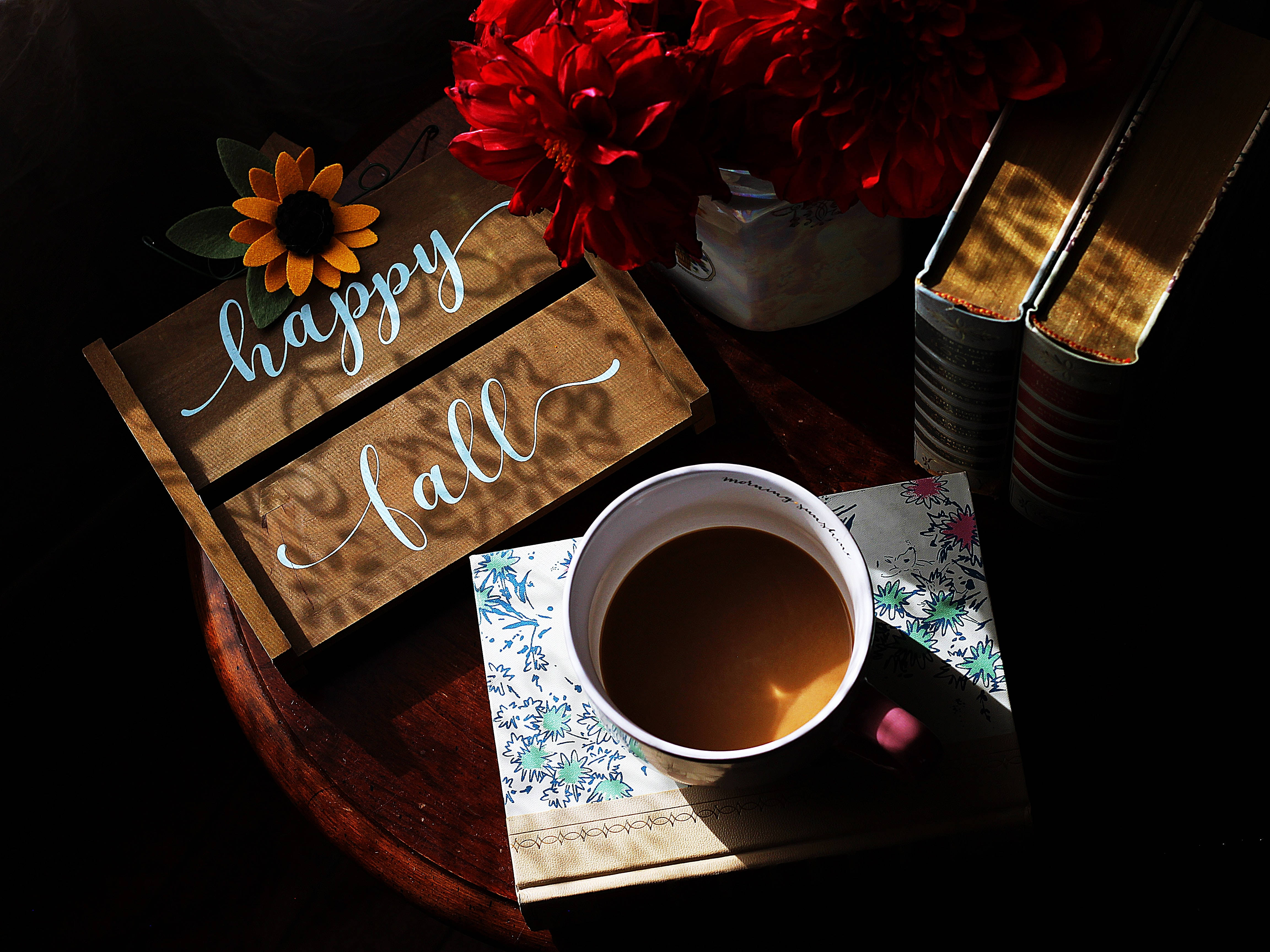 Cozy 桌布 壁紙 — 一個舒適的秋日靜物，有一杯咖啡、紅花、書籍和一個沐浴在溫暖陽光下的「happy fall」標誌。
