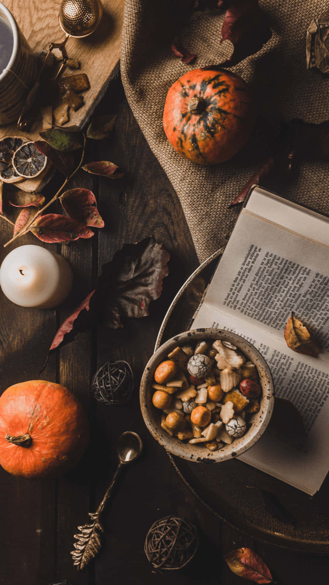 Fall 桌布 壁紙 — 一個舒適的秋日靜物，有南瓜、乾葉、堅果和一本打開的書，放在質樸的木桌上。