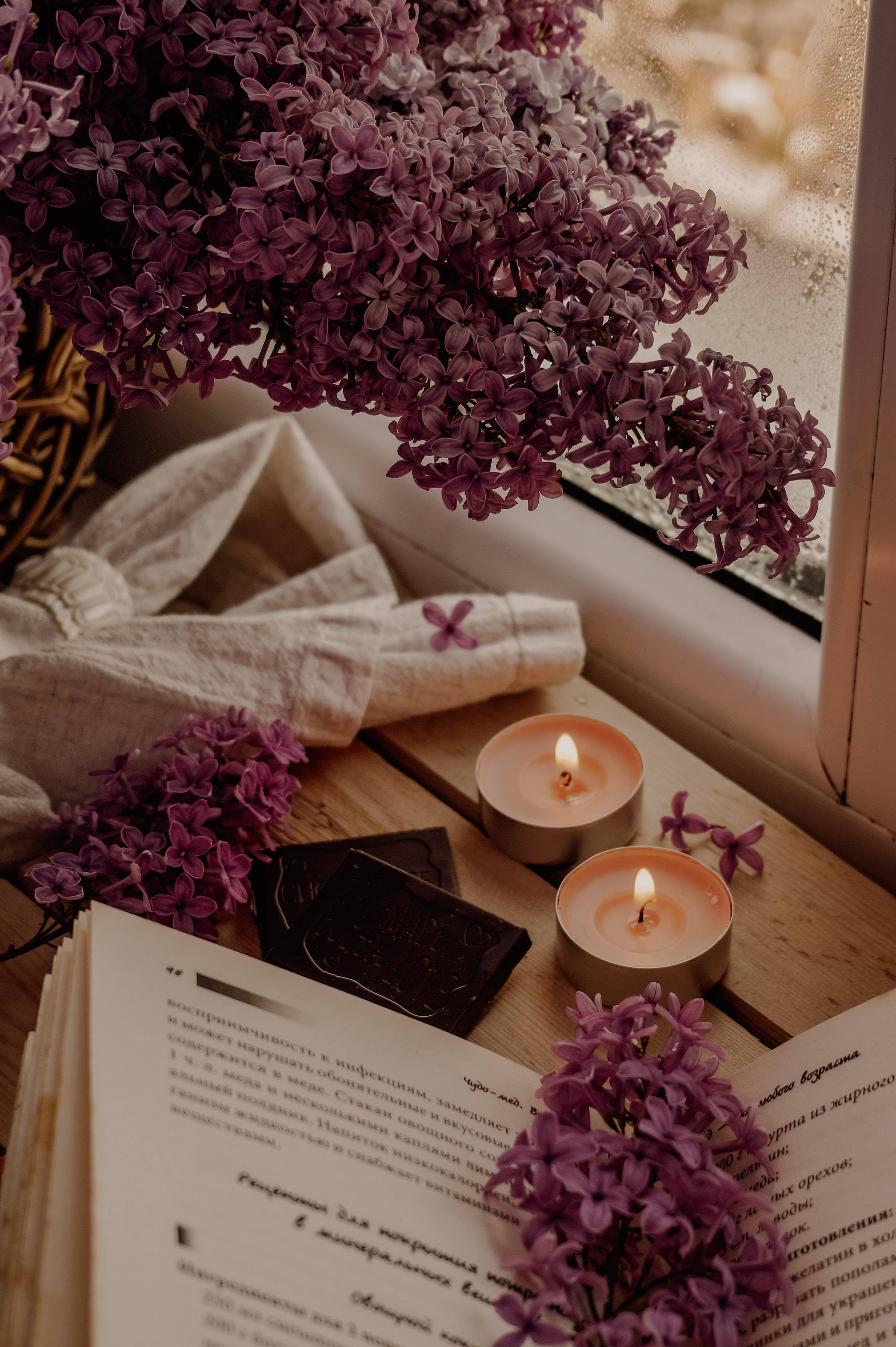 candles 桌布 壁紙 — 一個舒適的窗台場景，有紫色丁香蠟燭和一本打開的書，沐浴在柔和自然光中。