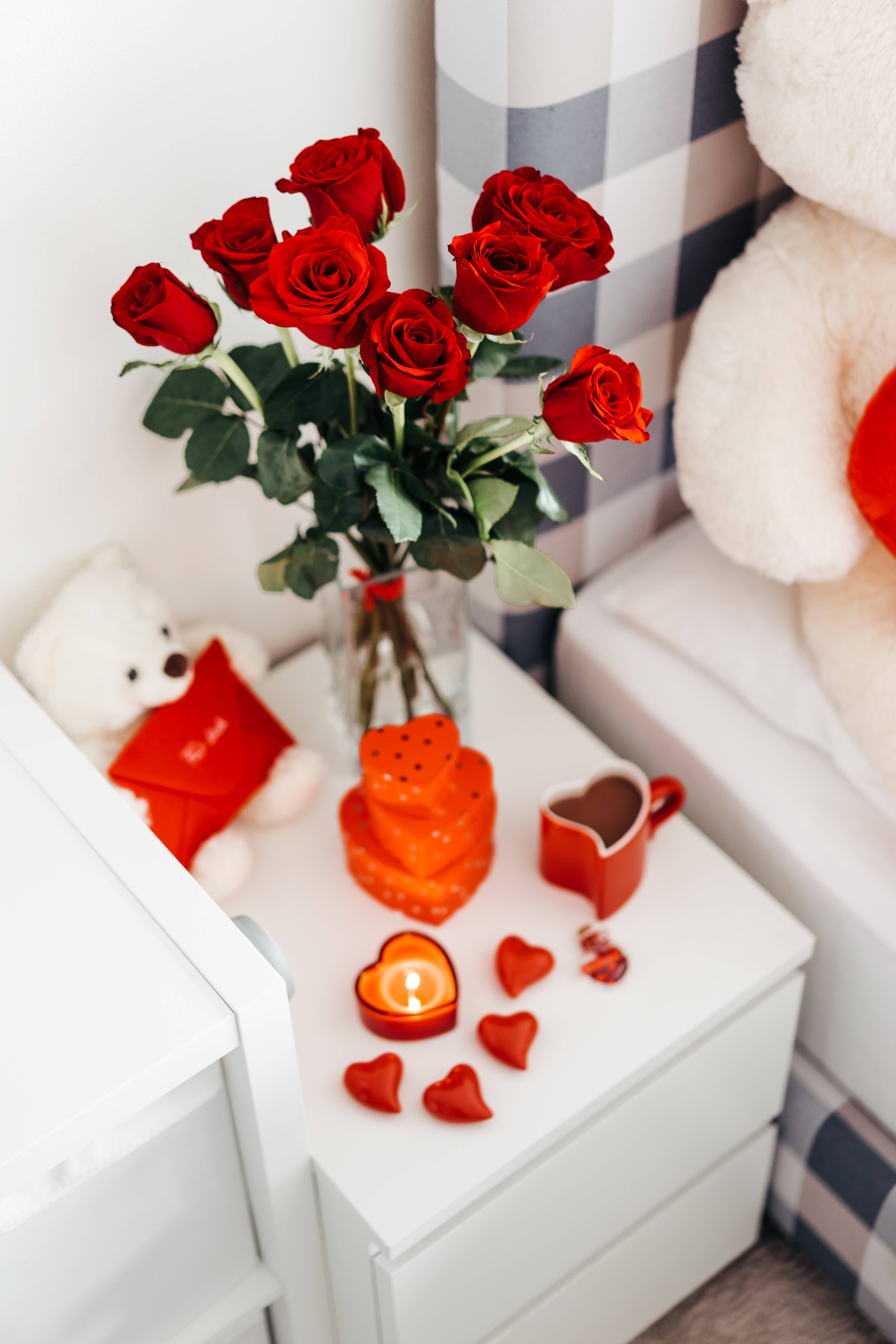 rose aesthetic phone 桌布 壁紙 — 一個舒適的臥室角落，白色床頭櫃上擺放著紅玫瑰、蠟燭和泰迪熊。